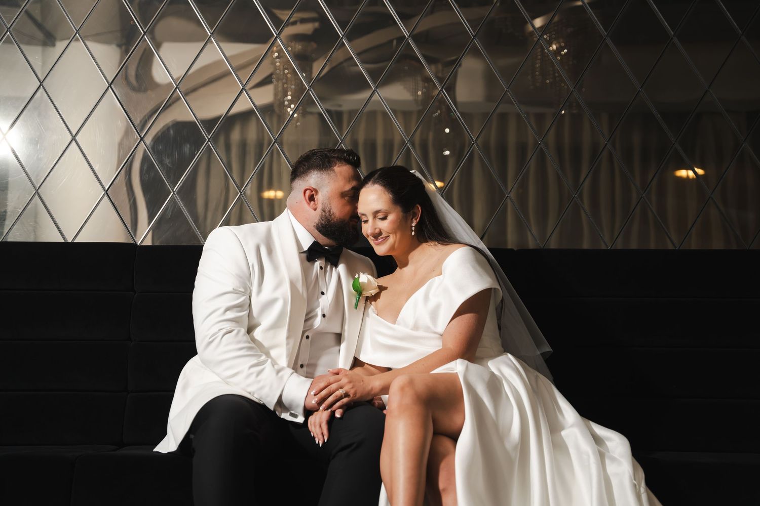 A couple in wedding attire dance together in an elegant ballroom setting with dramatic lighting.