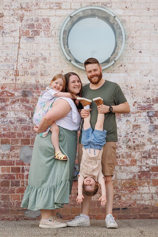 Fun family portrait against brick wall with circular window and upside down child.