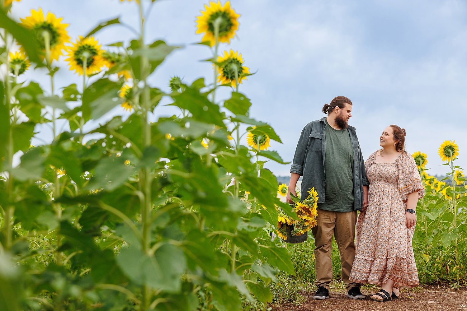 Couple standing together in a lush sunflower field on a sunny summer day.