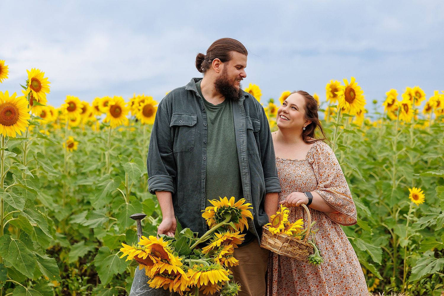 Two people share a tender moment in a blooming field of bright yellow sunflowers on an overcast day.