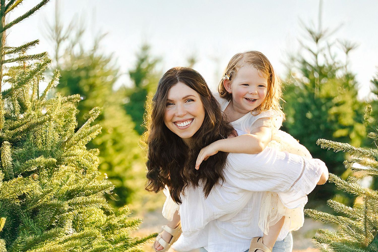 A parent and child share a joyful moment together among evergreen trees at a Christmas tree farm.