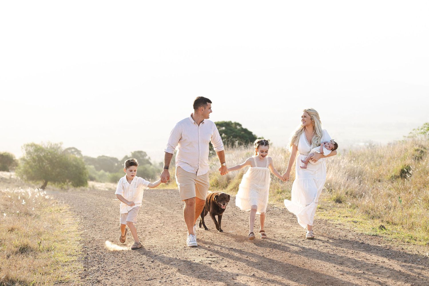 A family walks along a dusty desert trail with their dog during golden hour.