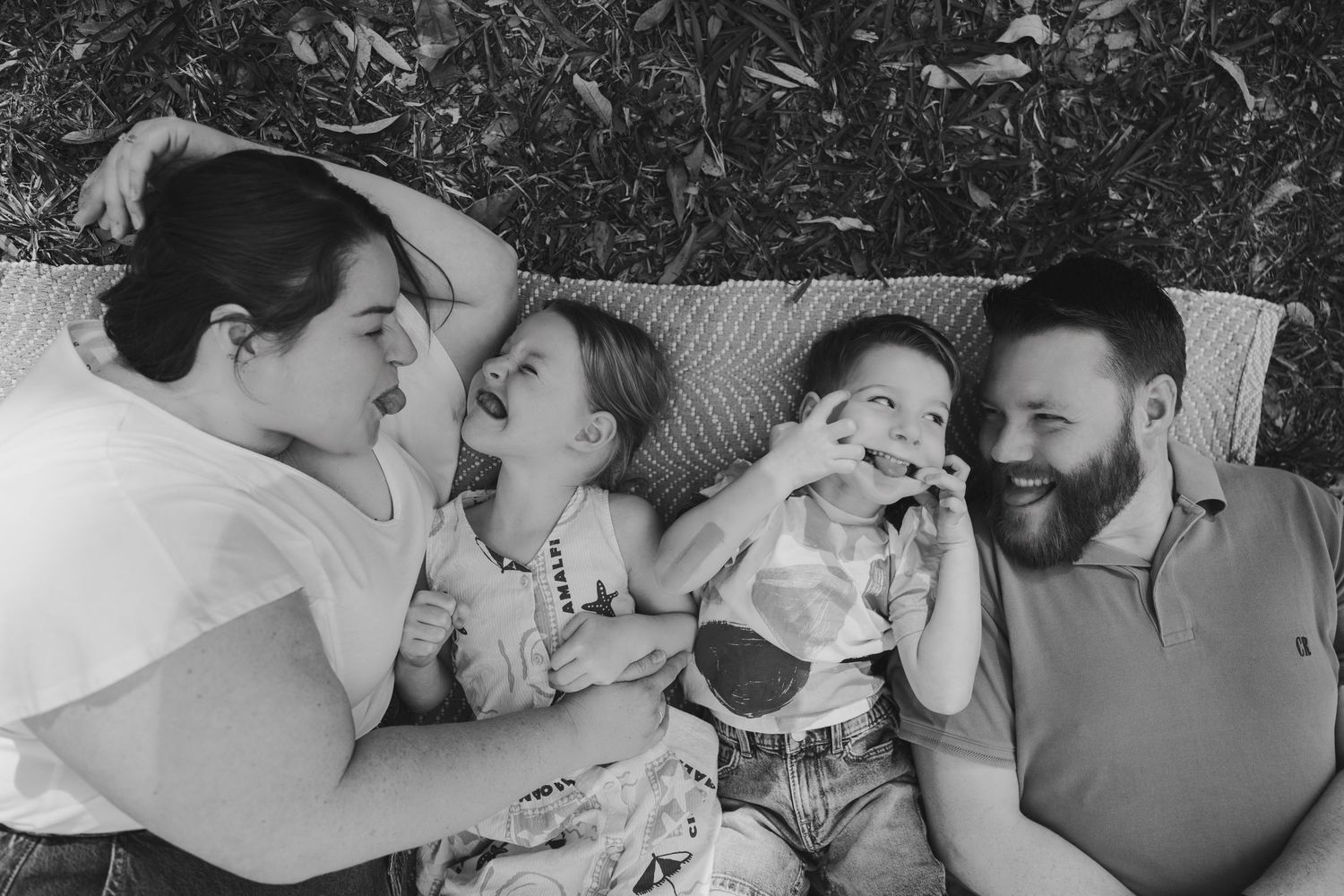 A happy family lying together outdoors on a blanket sharing playful expressions in black and white.
