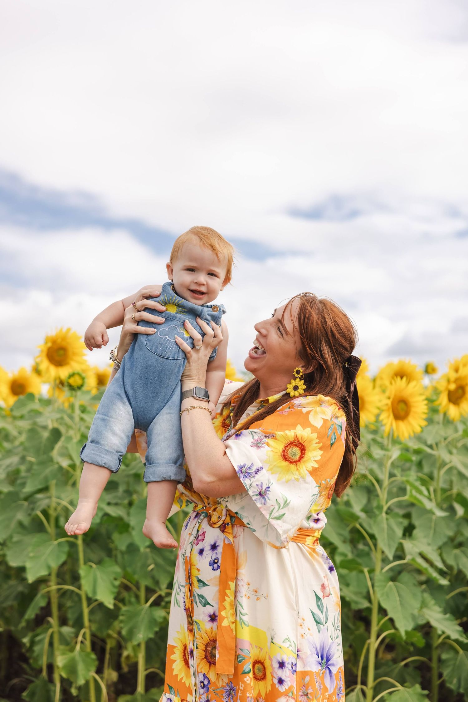 A joyful moment captured in a vibrant sunflower field with a floral dress against a cloudy summer sky.