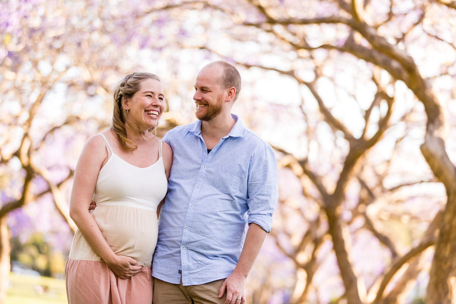A happy couple laughs together while walking through a beautiful spring garden with pink cherry blossoms blooming.