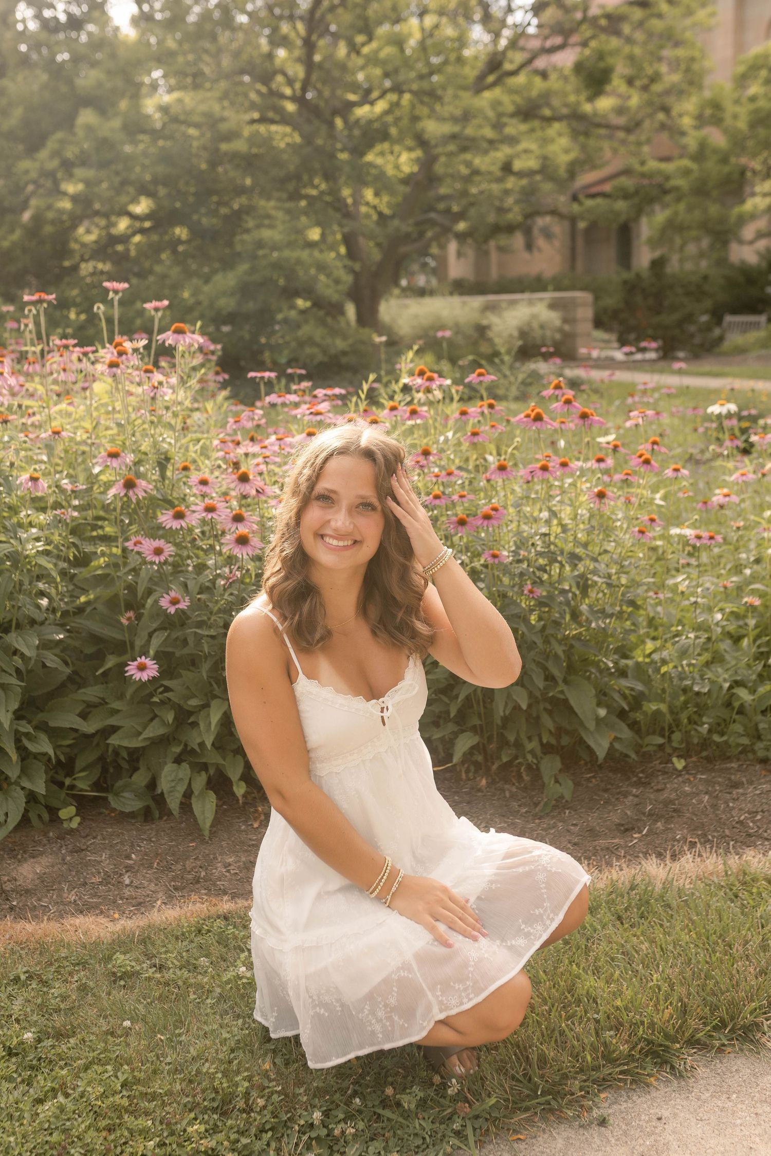 Senior kneeling in front of flower bed wearing white dress