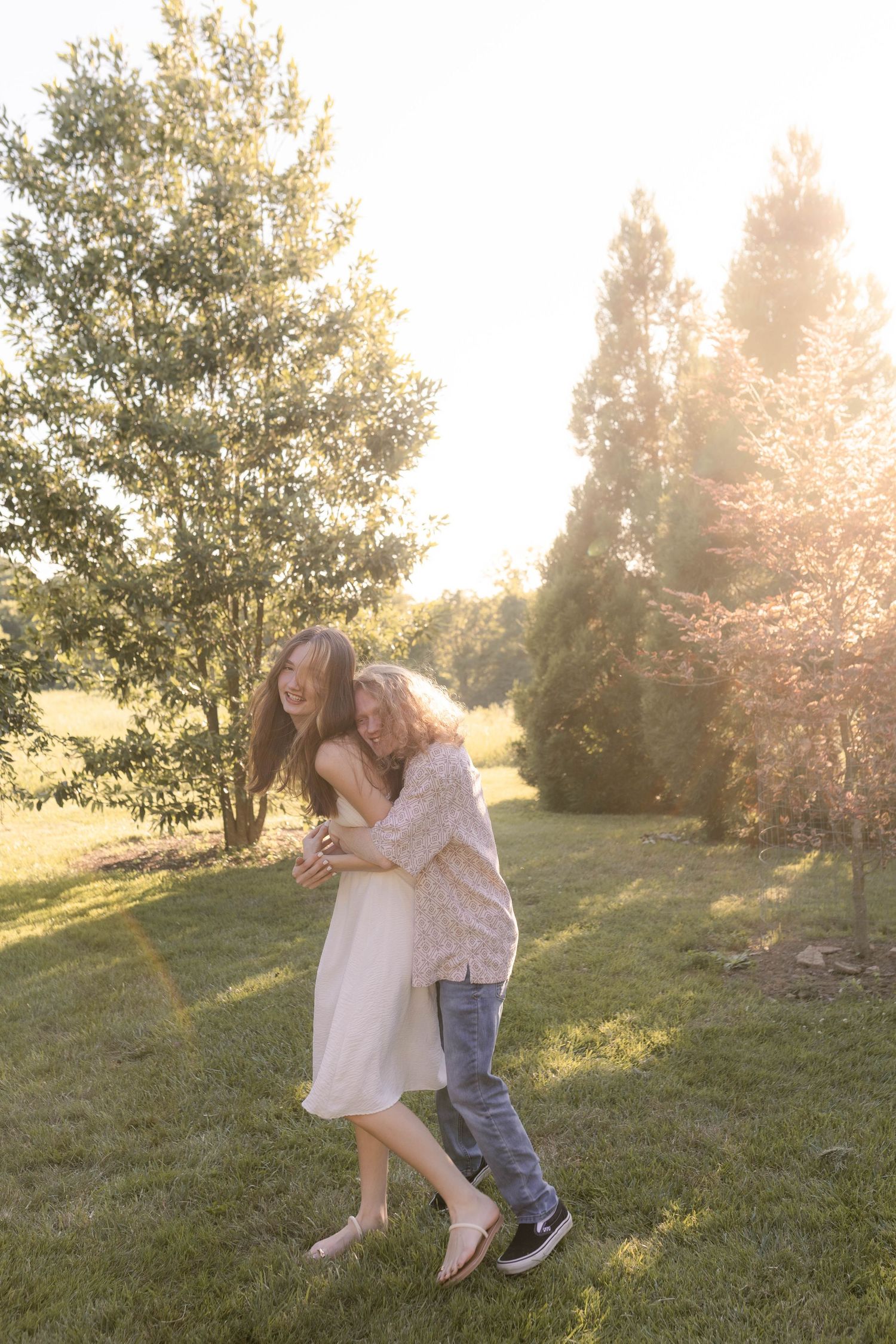 Couple standing together between trees during sunset engagement