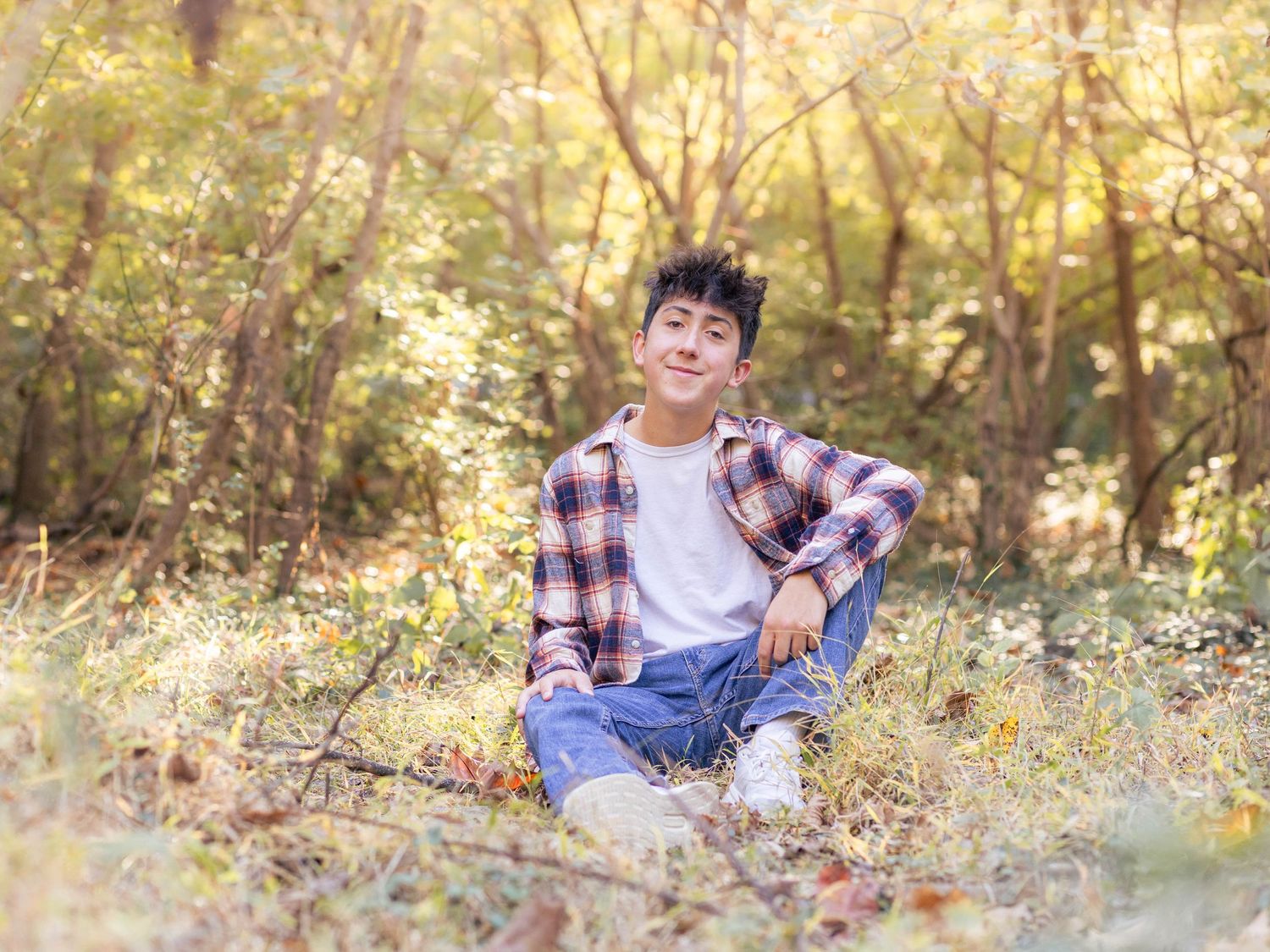 Teen boy posing in grassy forrest for senior pictures at golden hour