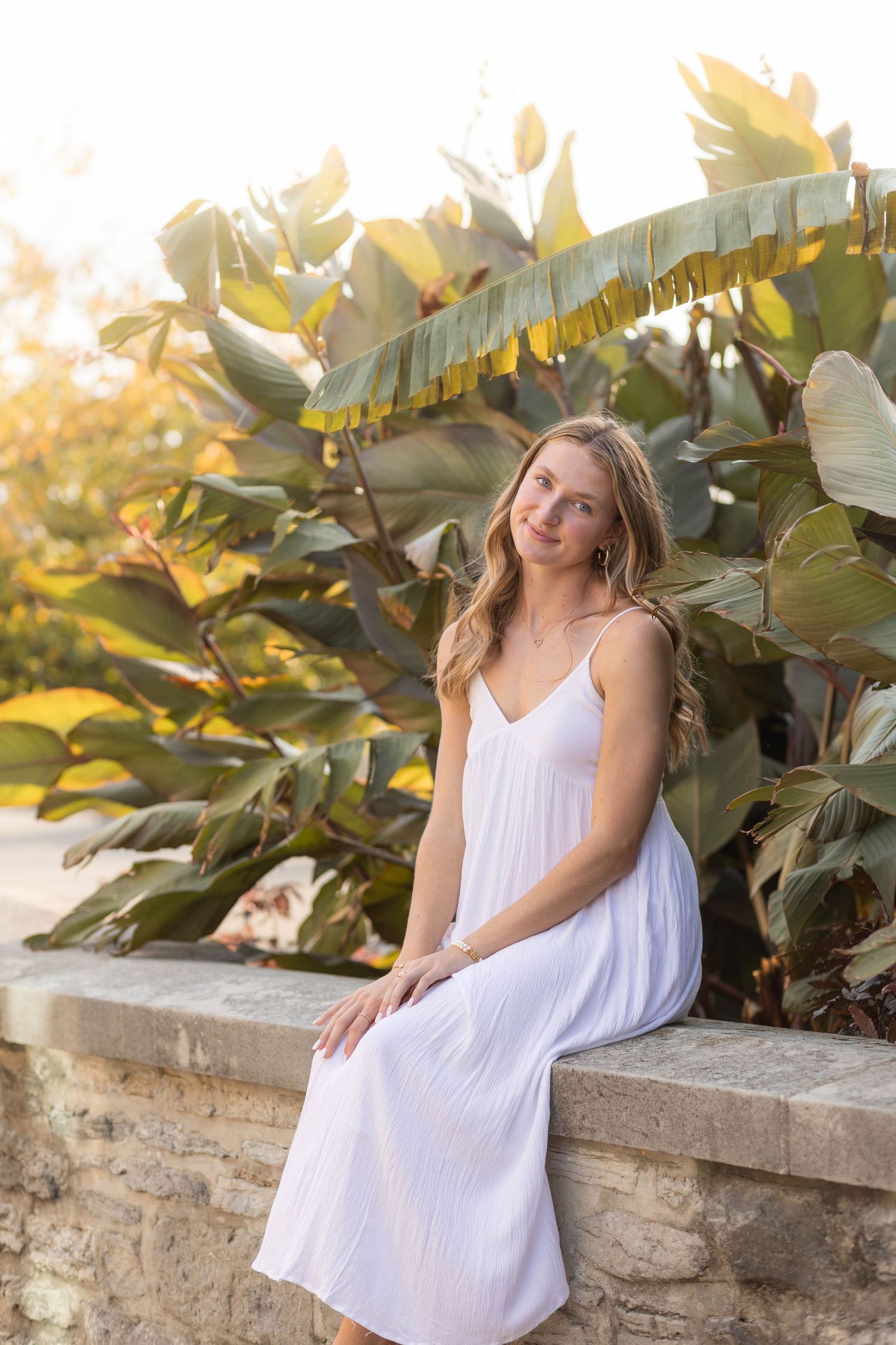 Senior girl sitting on stone wall in a park during sunset with a blurry natural background