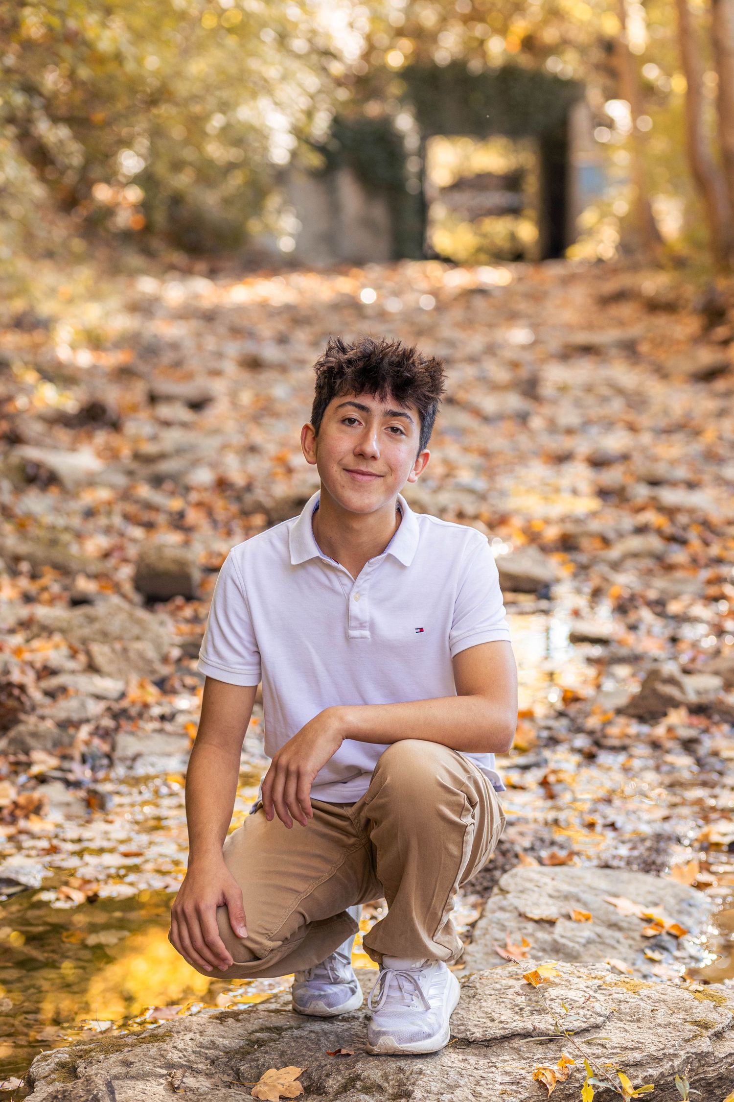Teen guy crouching in a rocky creek for senior pictures at golden hour