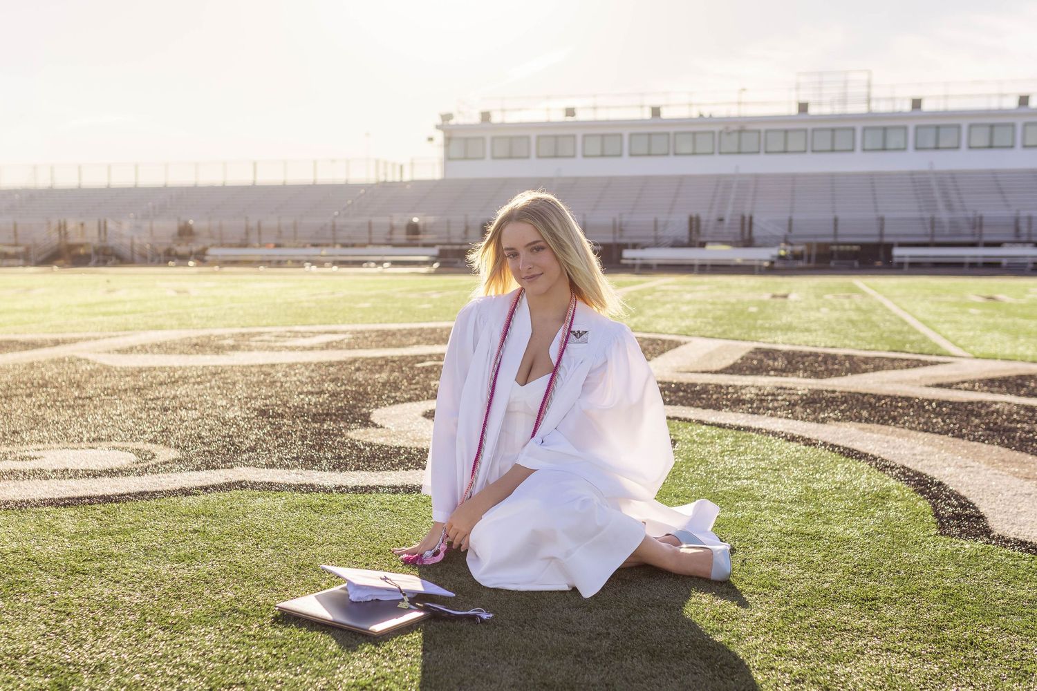 High school graduation photos on football field with cap, gown, and diploma