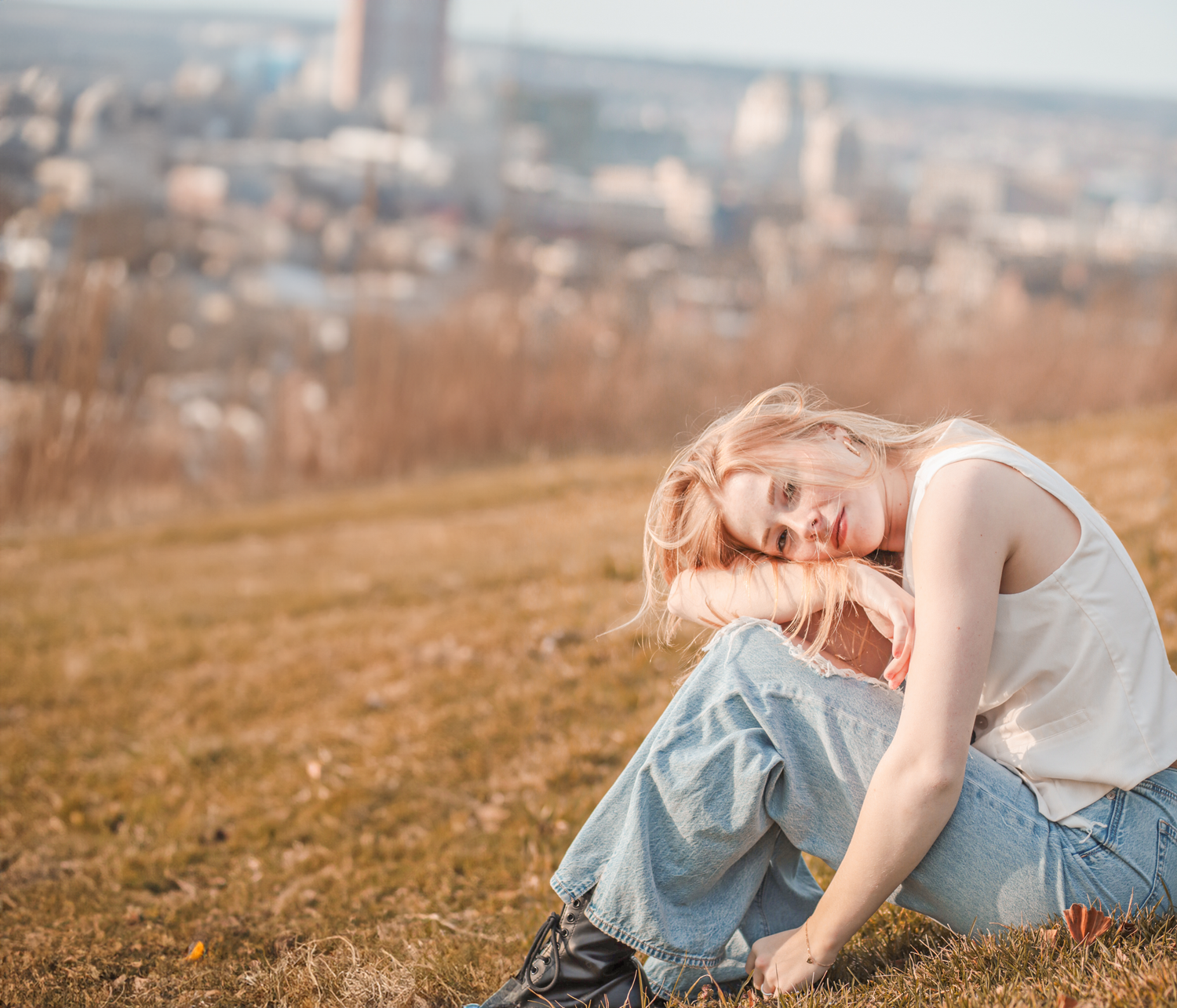 Girl sitting on hill with blurred city in the background for creative portraiture