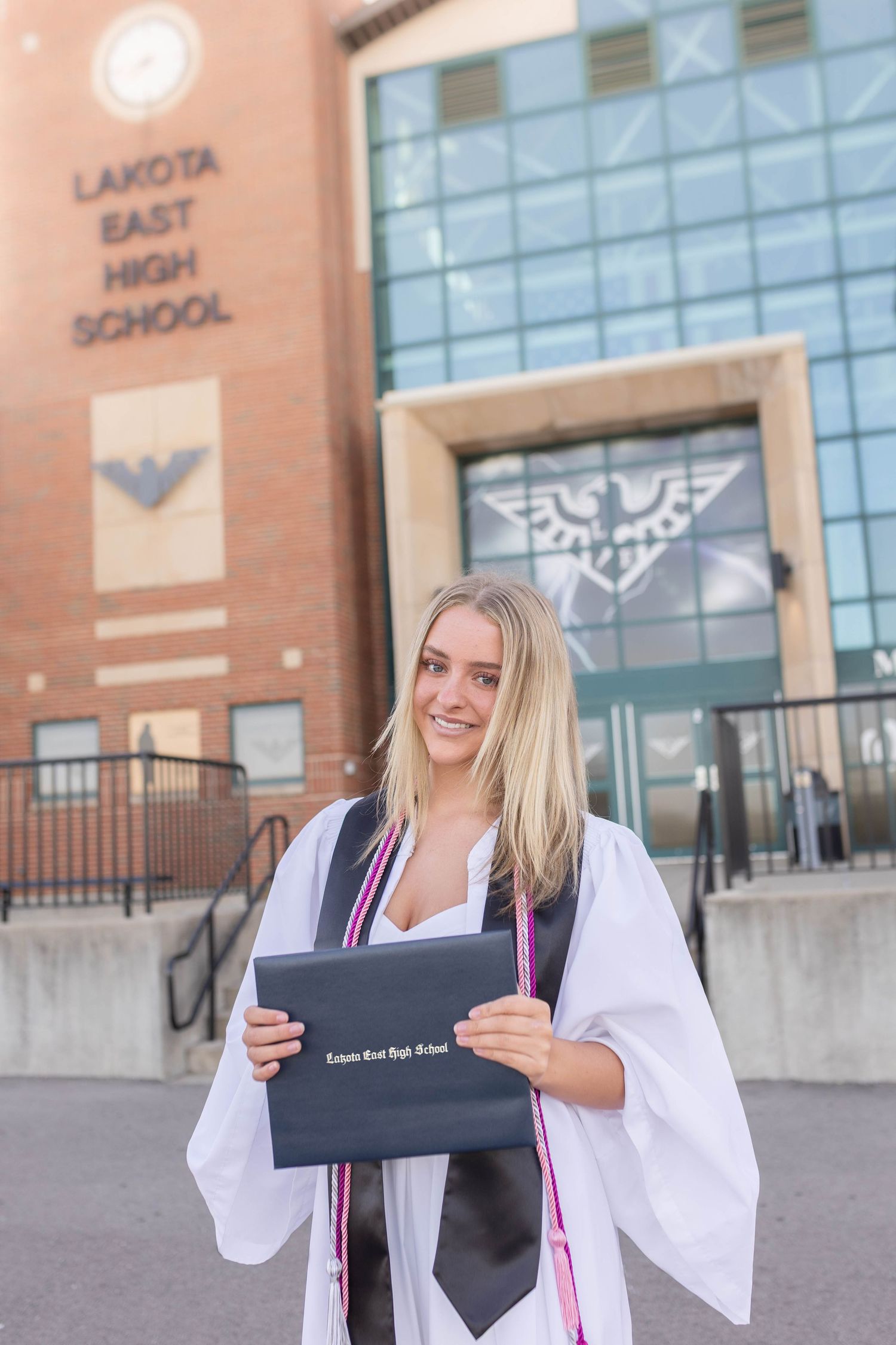High school graduation photos in front of school with cap, gown, and diploma