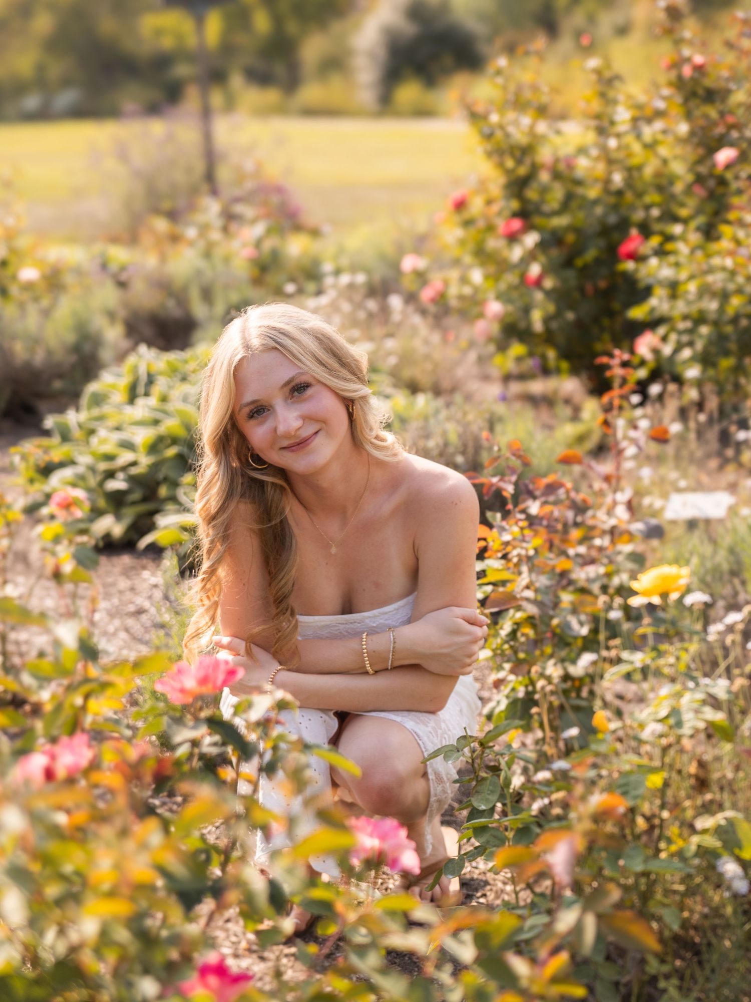Senior girl smiling in flower bed at sunset with a soft glow