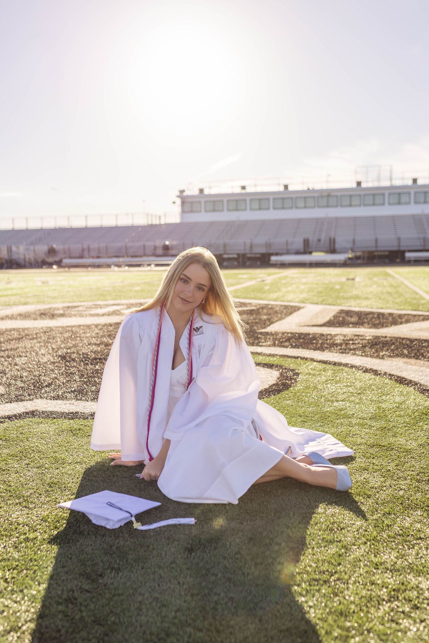 High school graduation photos on football field with cap, gown, and diploma