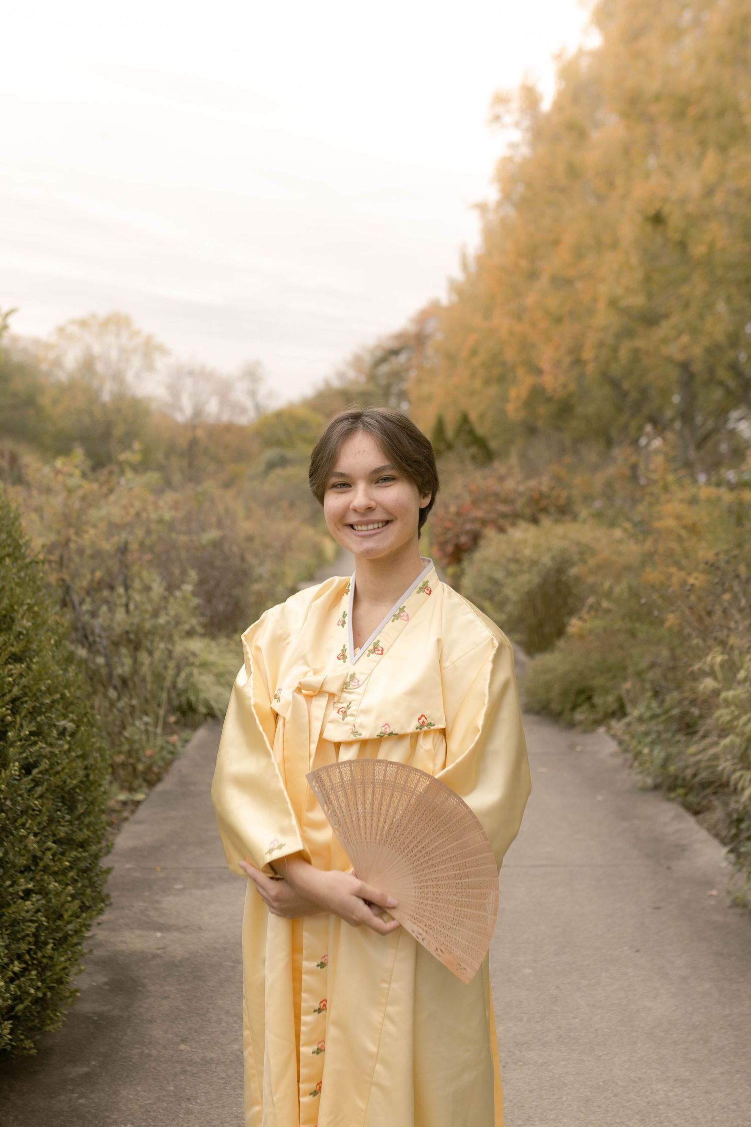Senior wearing traditional dress with fan in park during fall