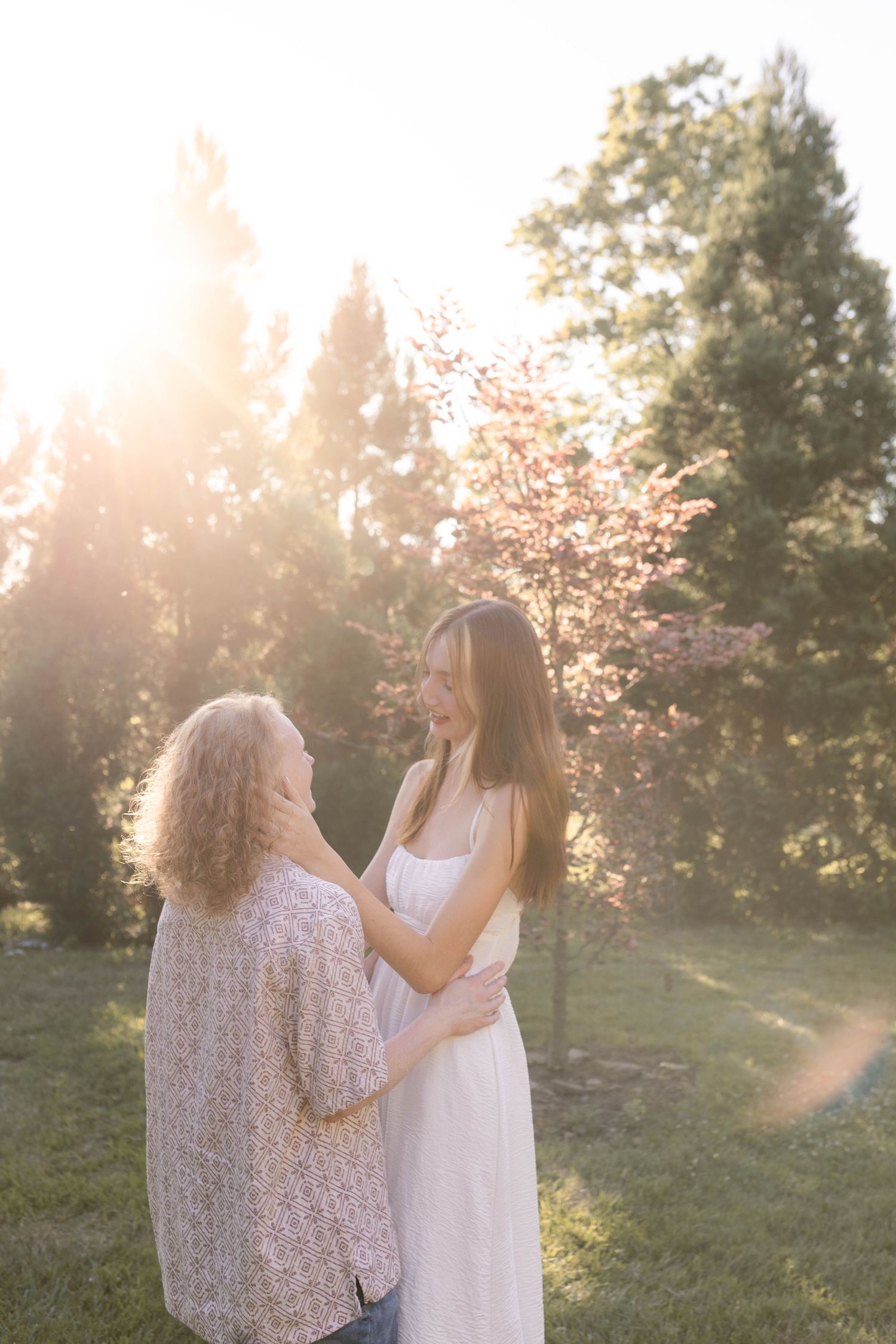 Couple standing together between trees during sunset engagement