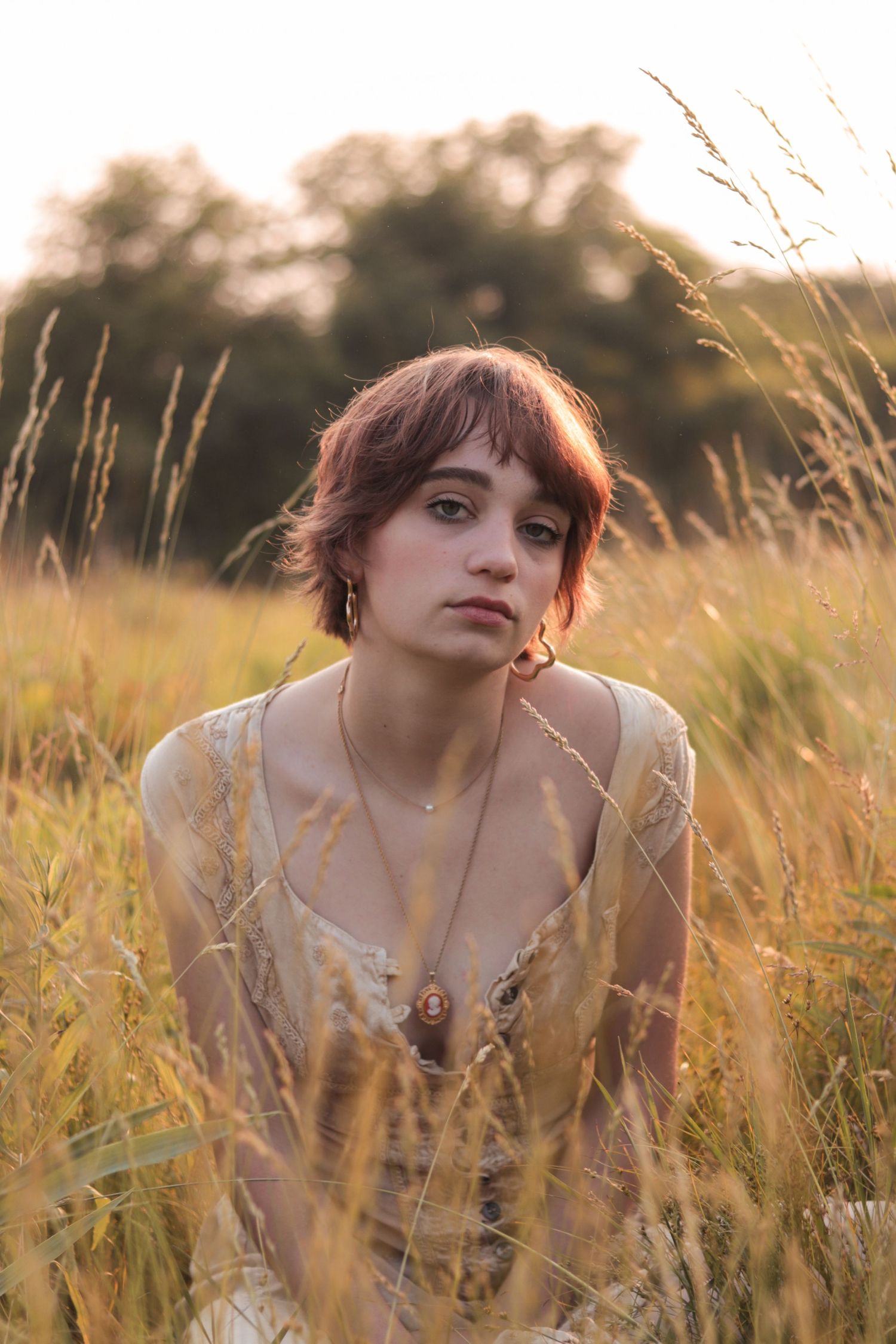 Person posing in park for editorial photo with tall grass and blurry background at sunset