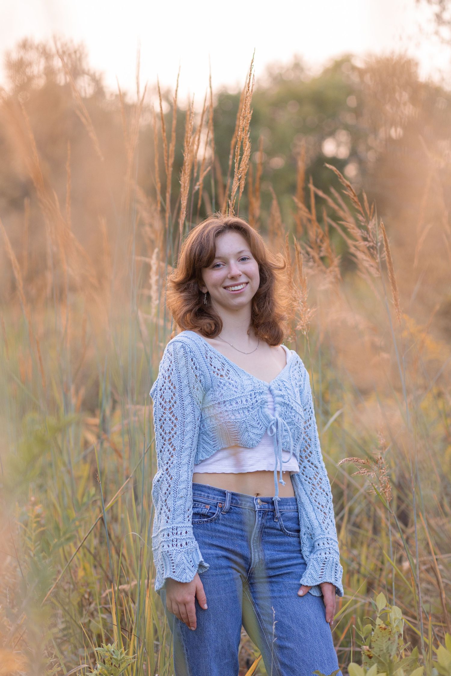 Senior girl smiling in grassy field at sunset with natural light