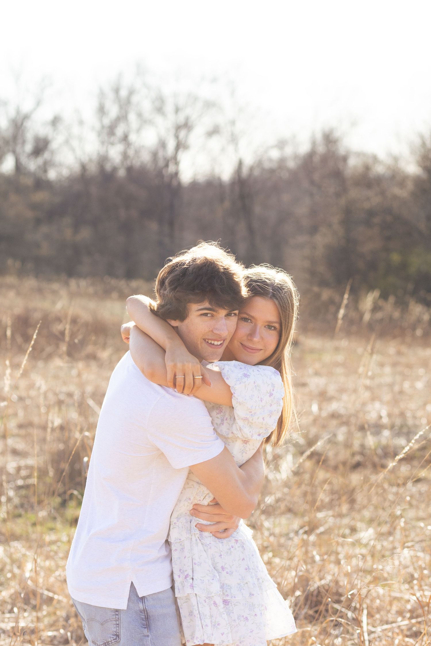 Couple smiling and embracing in grassy field with a warm glow