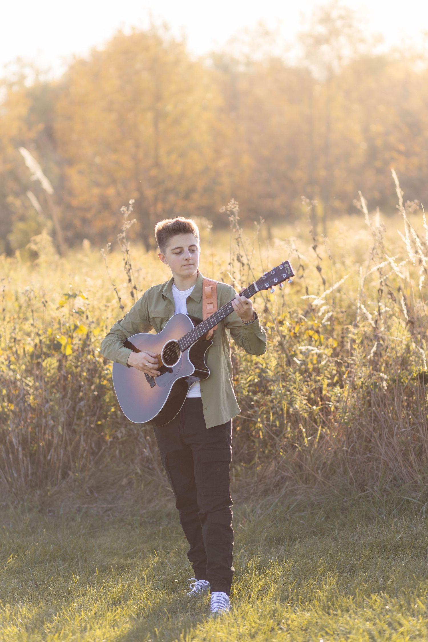 Senior posing in field during sunset with guitar and music accessories