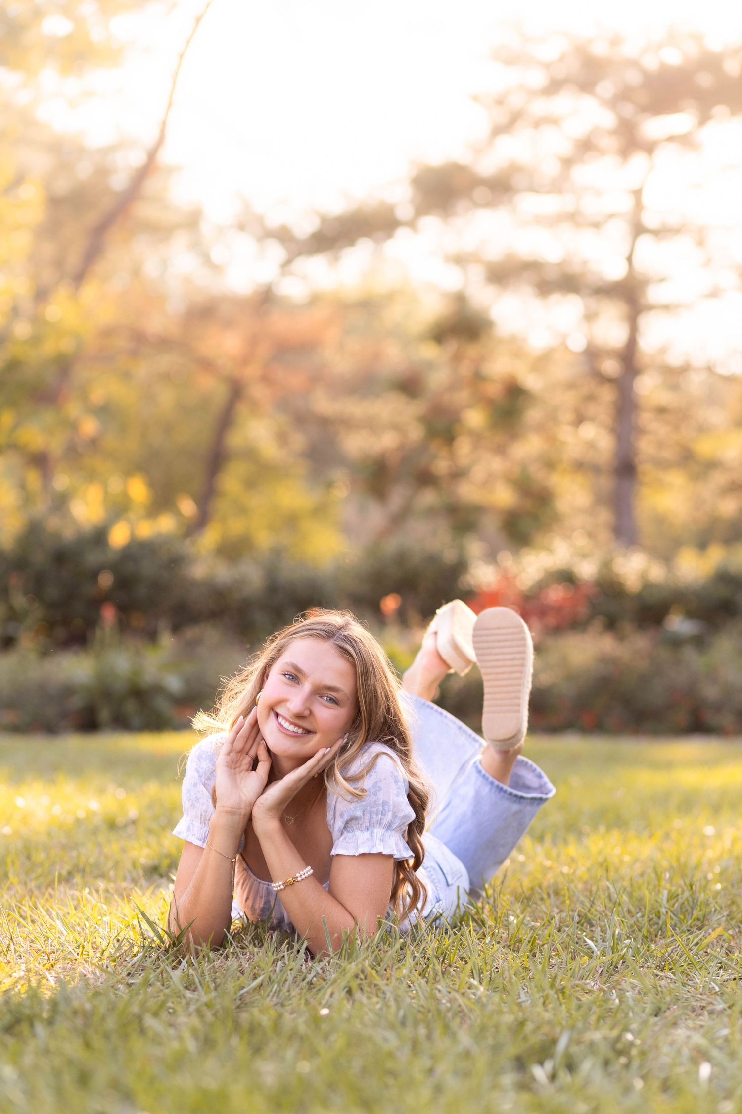 Senior girl wearing casual clothes laying on the grass in park with soft glow behind