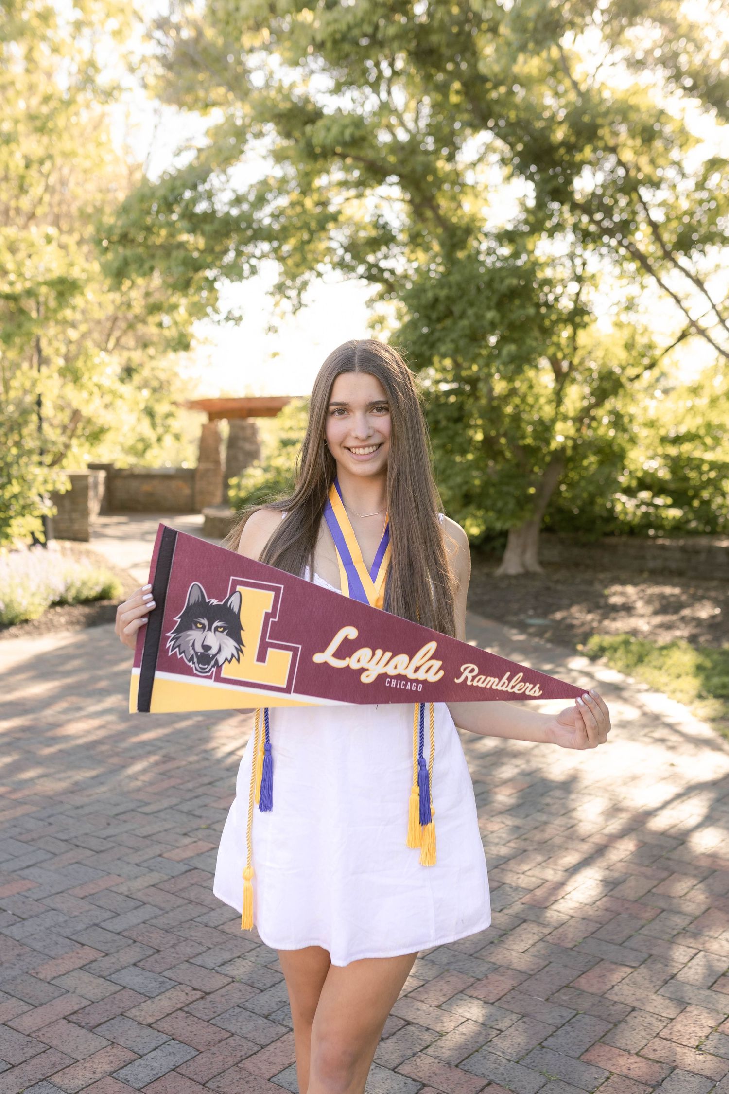 Senior girl wearing white dress and holding college pennant in park