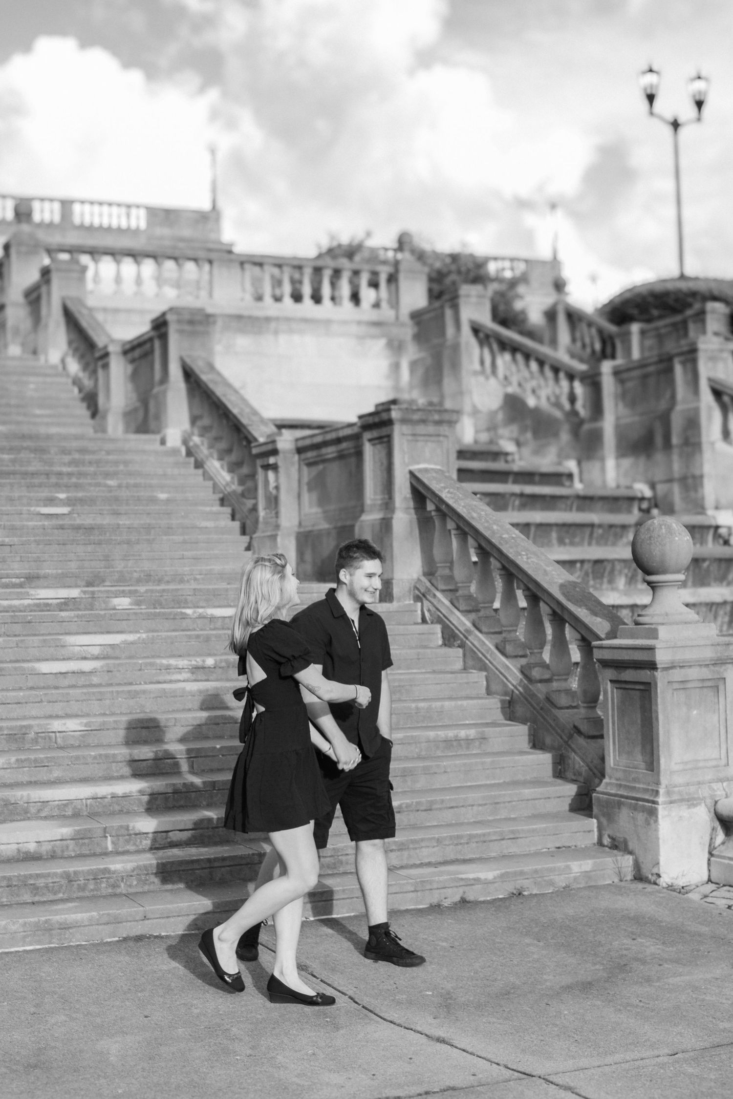 Black & white photo of couple walking in front of stone steps and fountain in park
