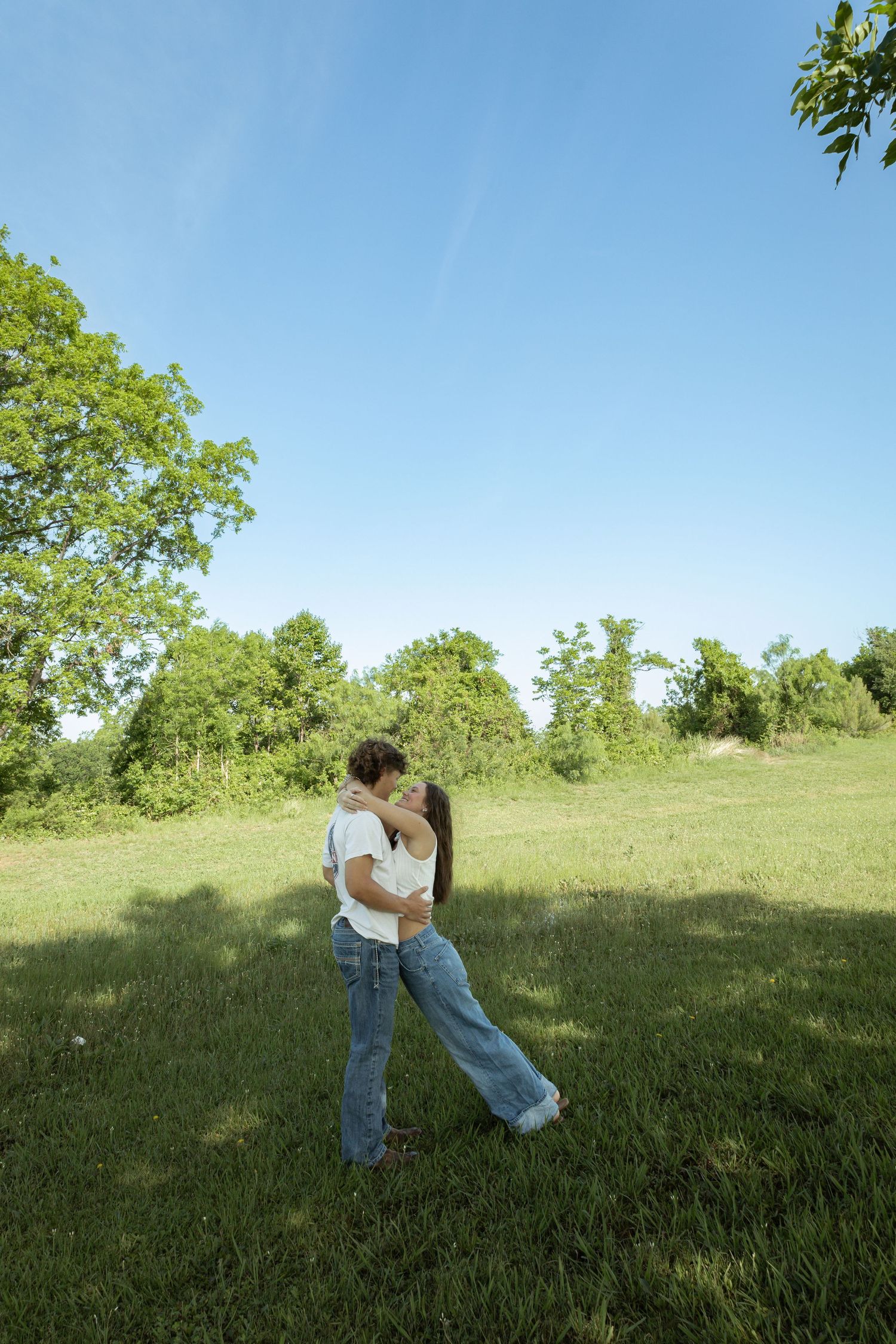 A couple sharing a romantic kiss in a lush green park under a clear blue sky on a sunny day.