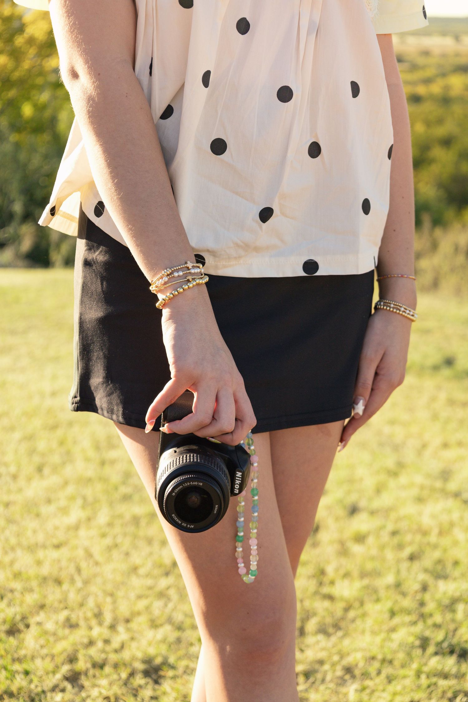 Female photographer holding a Nikon DSLR camera at her side in a grassy outdoor setting.