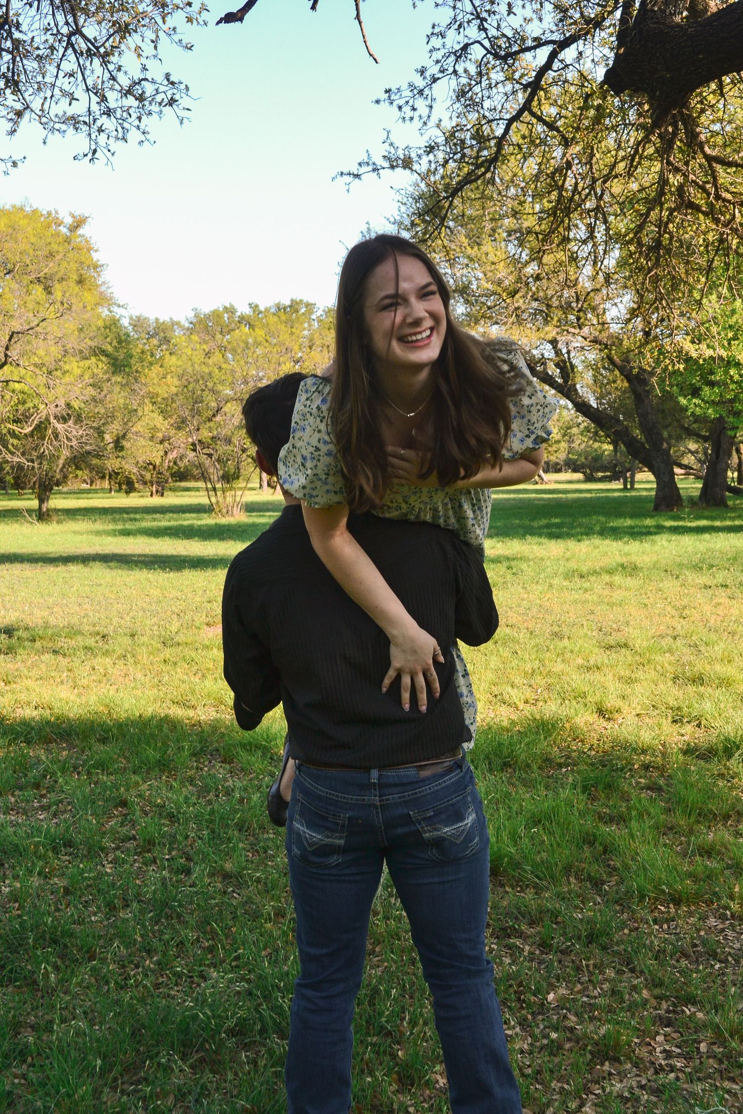 Young woman laughing while getting a piggyback ride outdoors in a sunny green park.