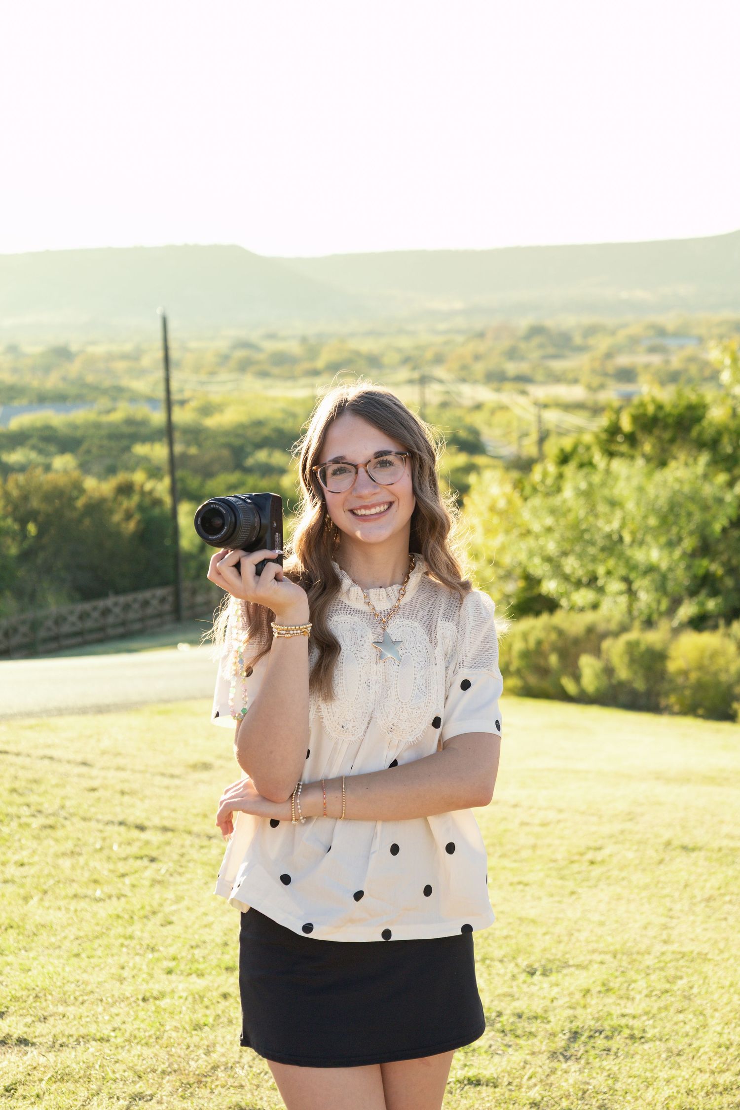 Smiling young female photographer holding a Nikon camera outdoors at golden hour.
