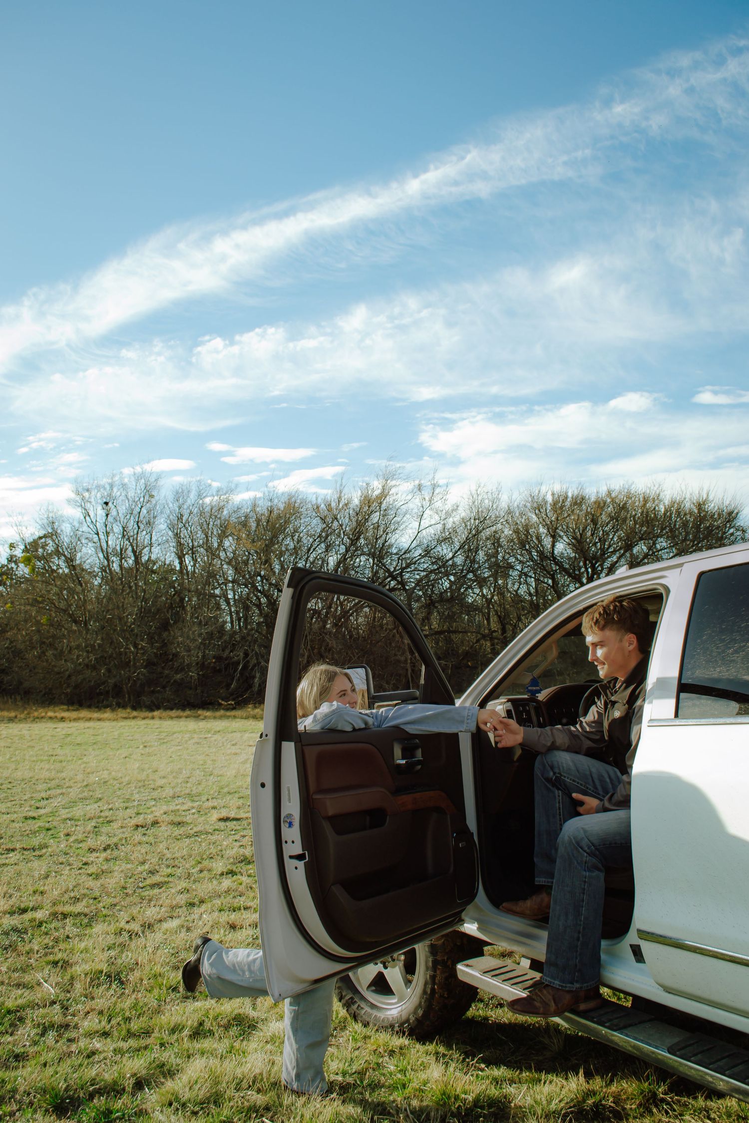 Young couple sharing a tender moment by a white pickup truck door in a sunny open field.