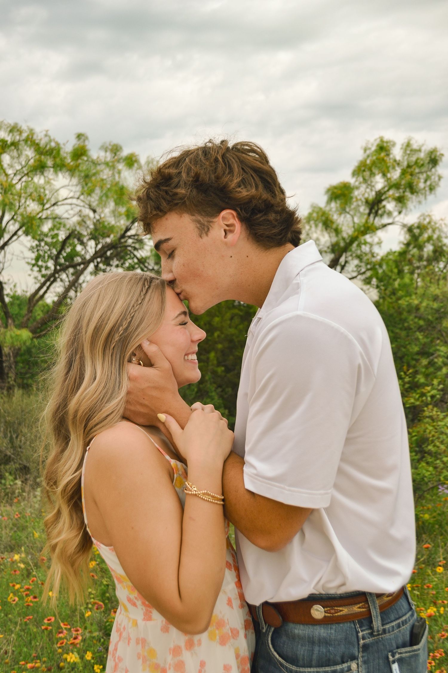 Young couple sharing a tender forehead kiss in a wildflower field under a cloudy sky.