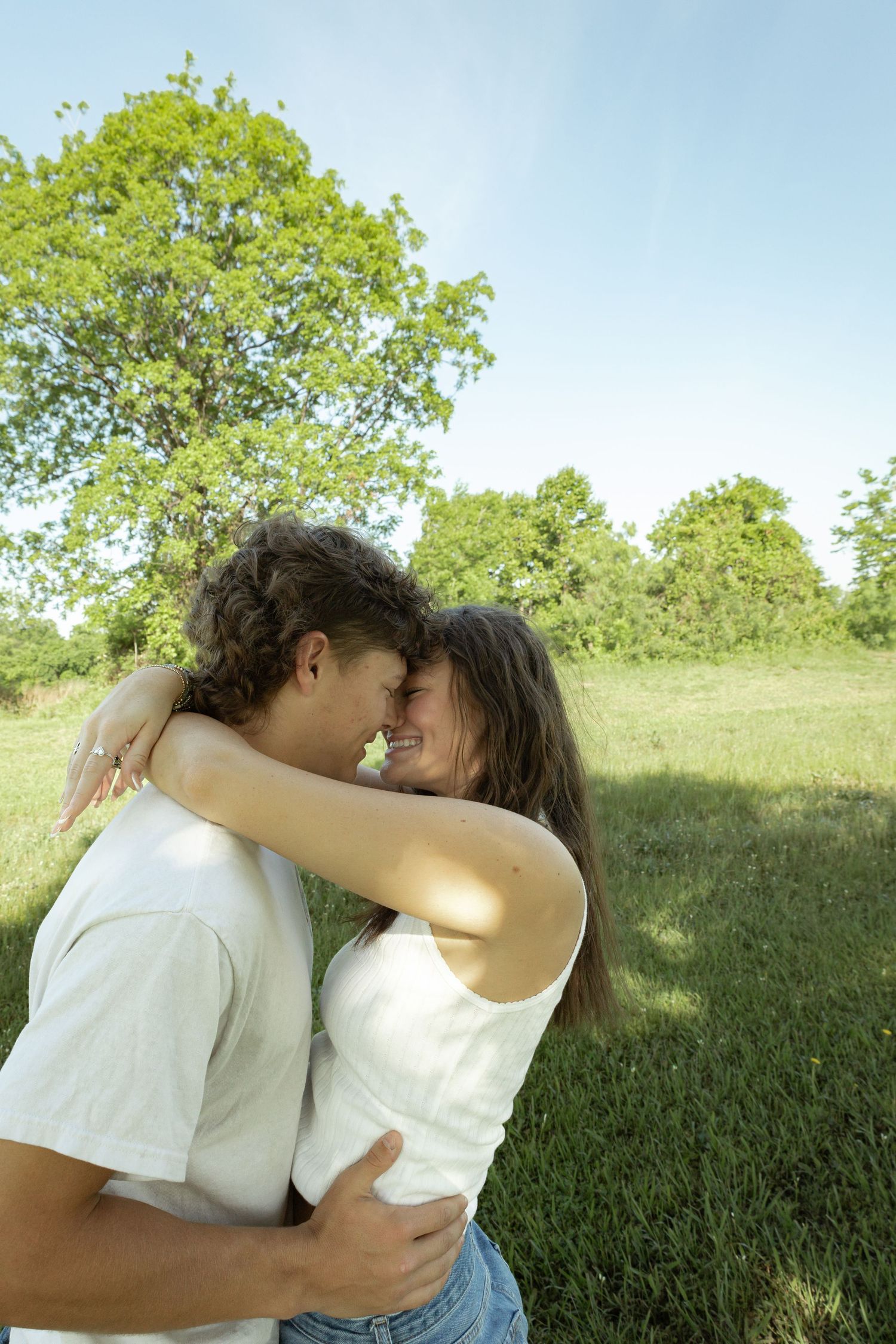 Young couple embracing and touching foreheads affectionately outdoors in a lush green park on a sunny day.