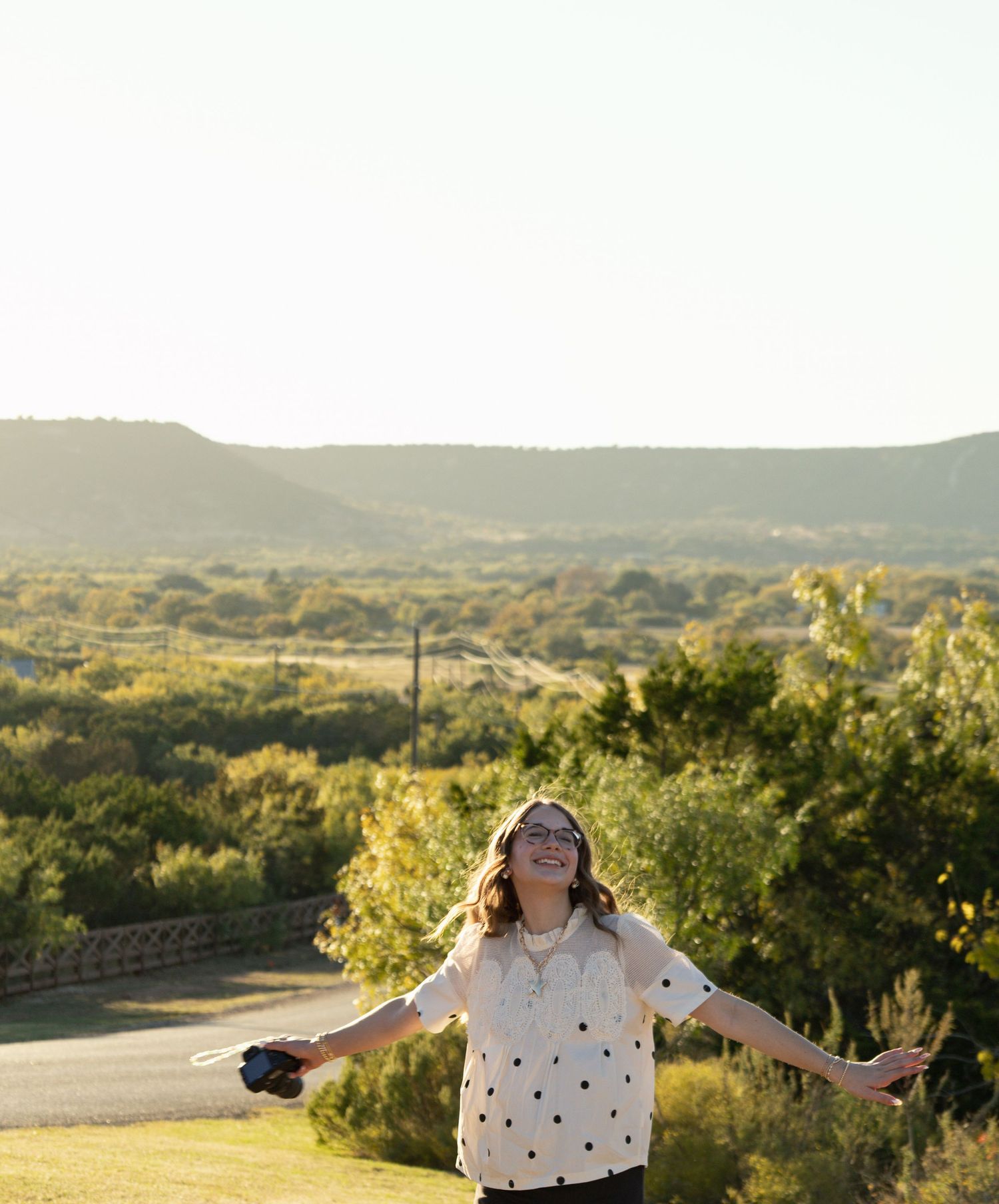 Happy young female photographer with open arms enjoying a beautiful sunny outdoor landscape.