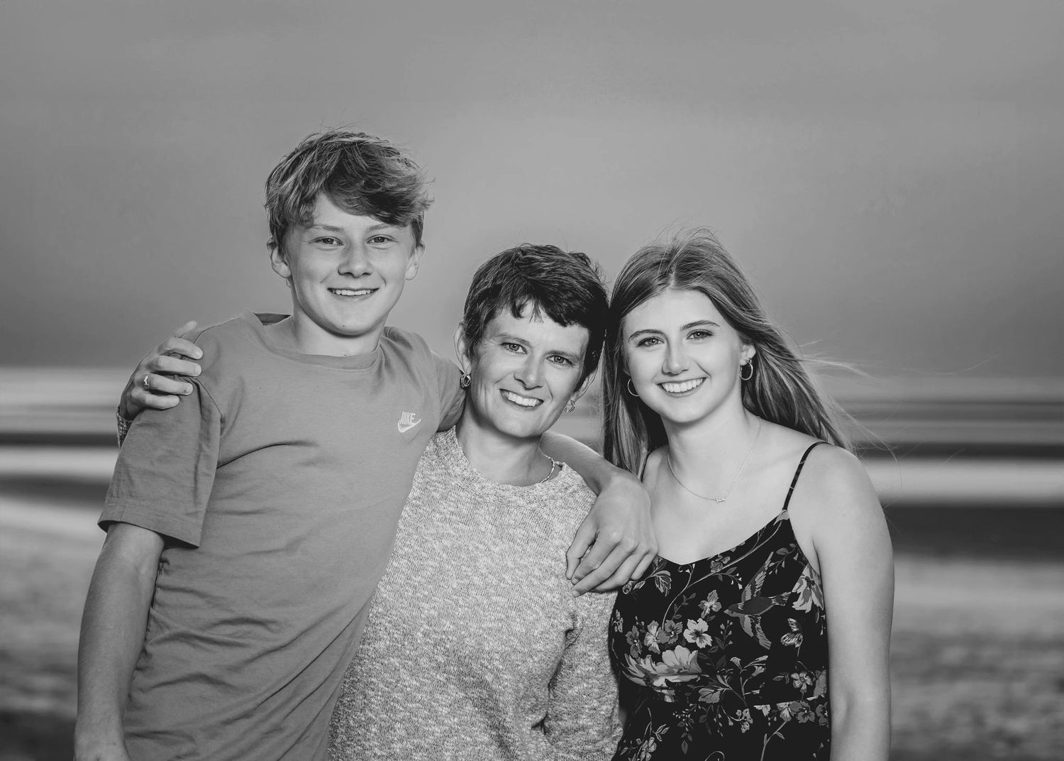 Black and white portrait of three people smiling together at the beach.
