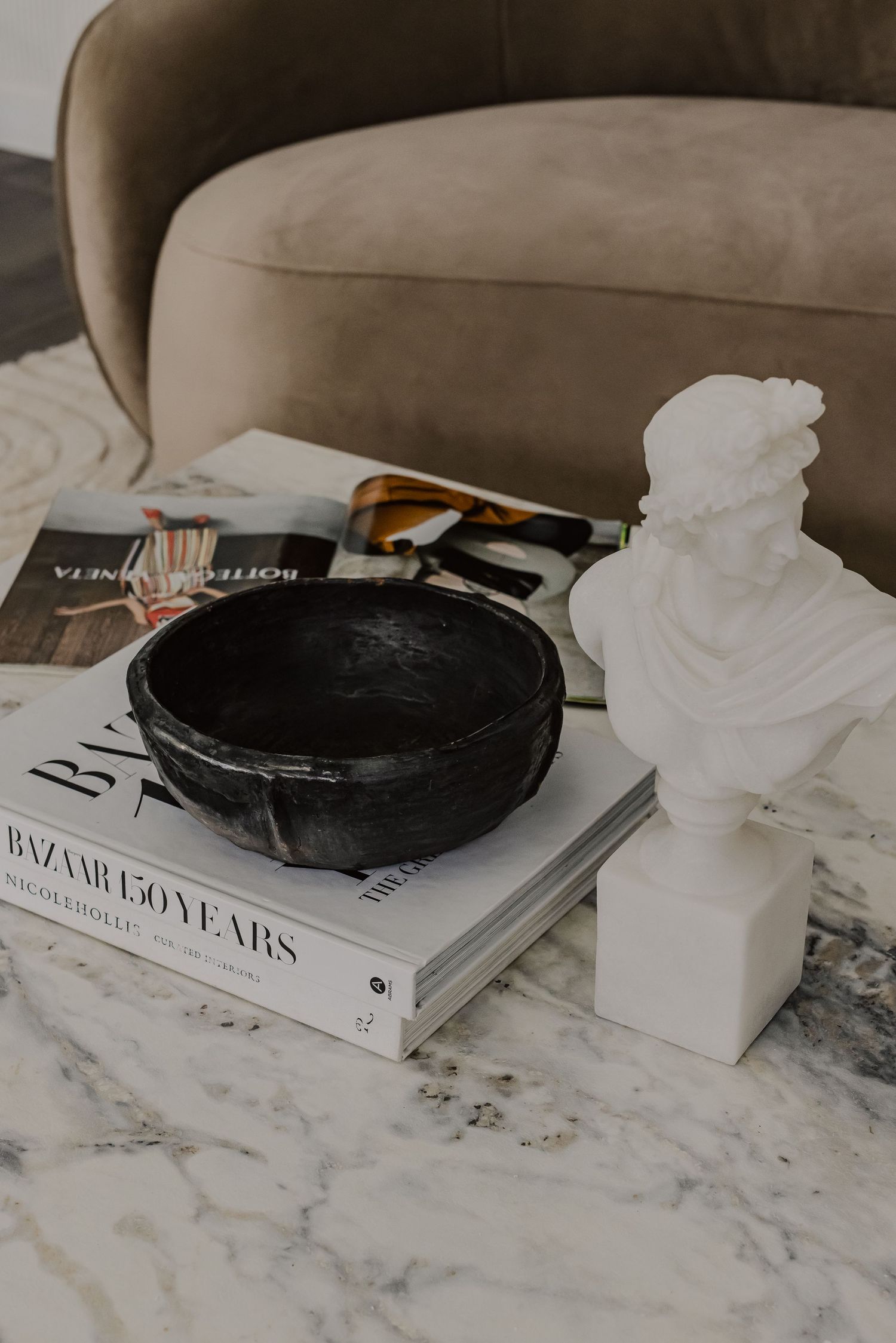 A marble coffee table styled with fashion books, black candle holders, and white ceramic decor pieces.