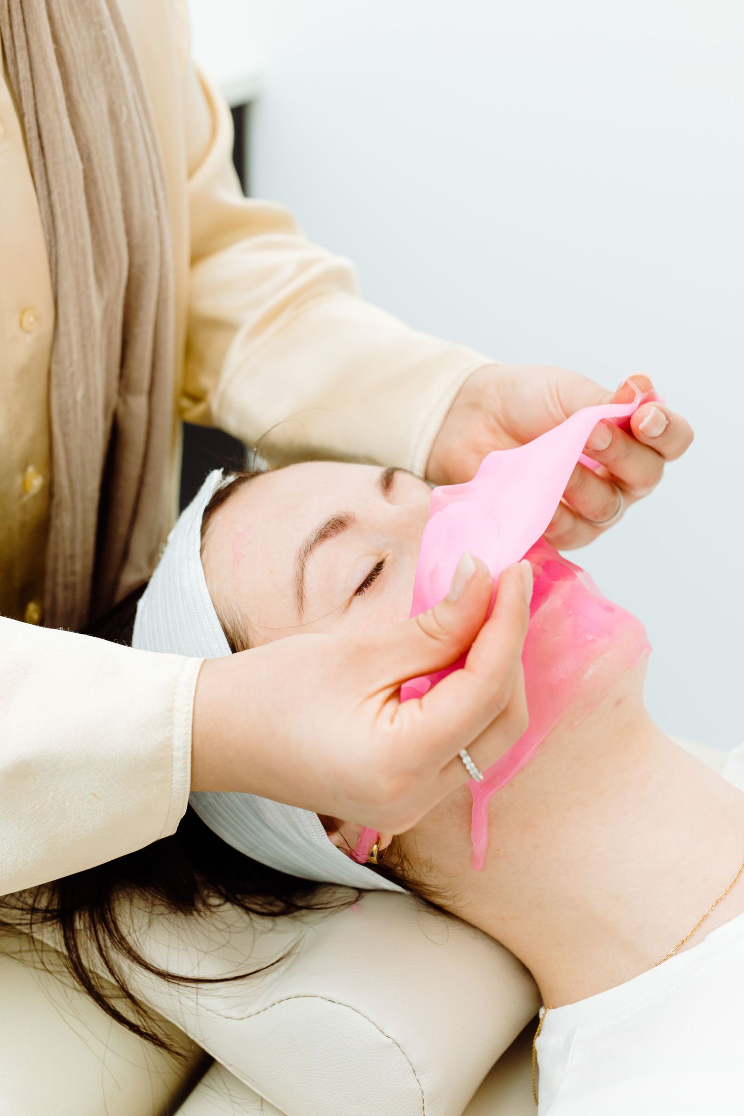 A person receiving a pink facial treatment while lying down with eyes closed on a spa table.