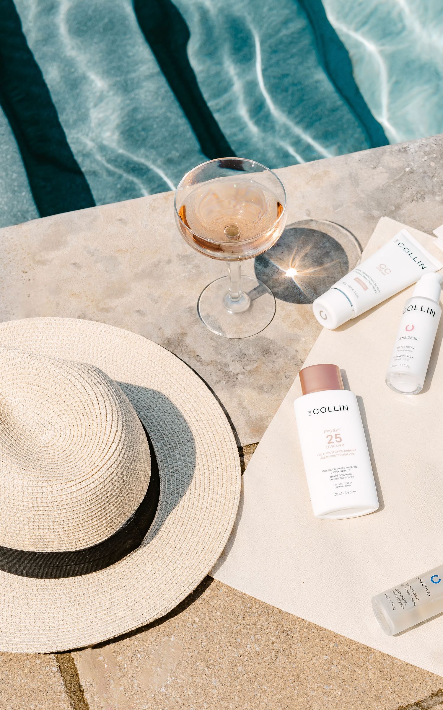 A collection of beige straw sun hats and wine glasses arranged beside a pool with shimmering turquoise water.