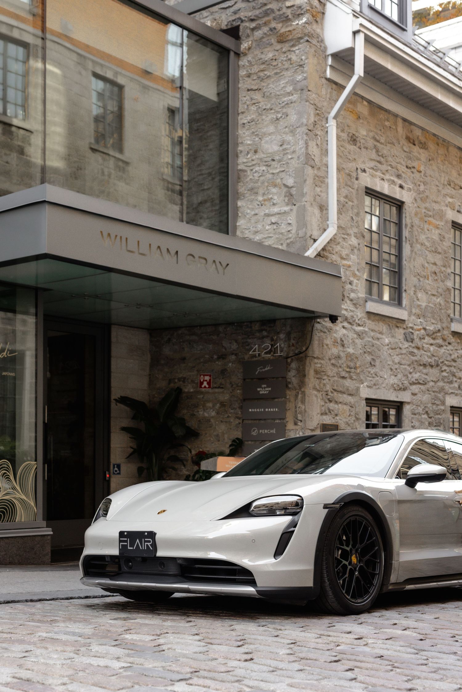 White Porsche Taycan parked on cobblestone street outside William Gray hotel with stone building facade.