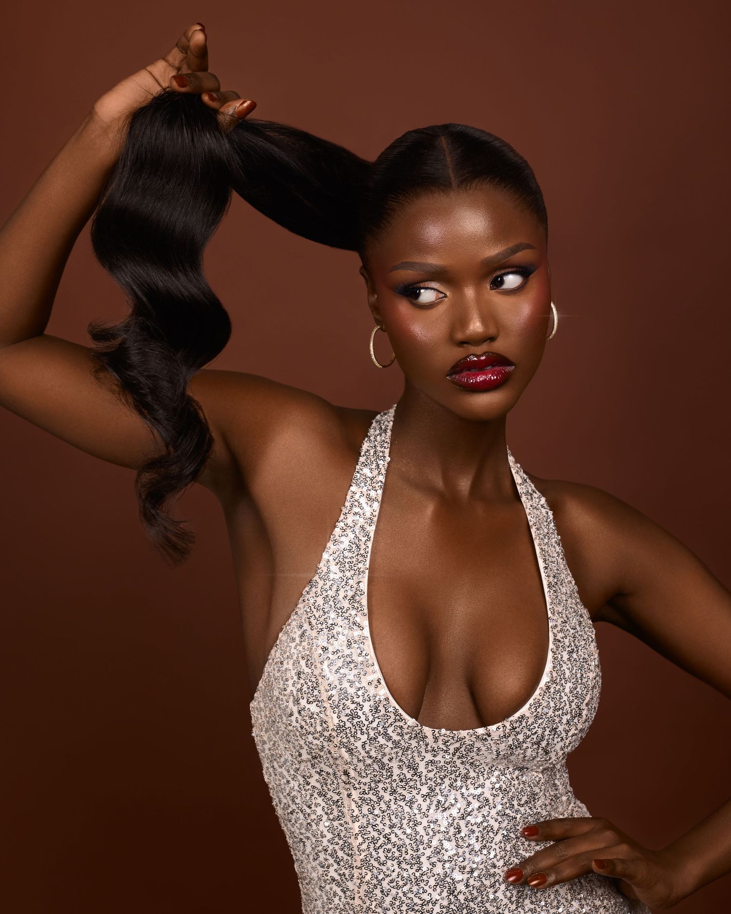 Glamorous fashion portrait with sparkling halter dress against brown background.
