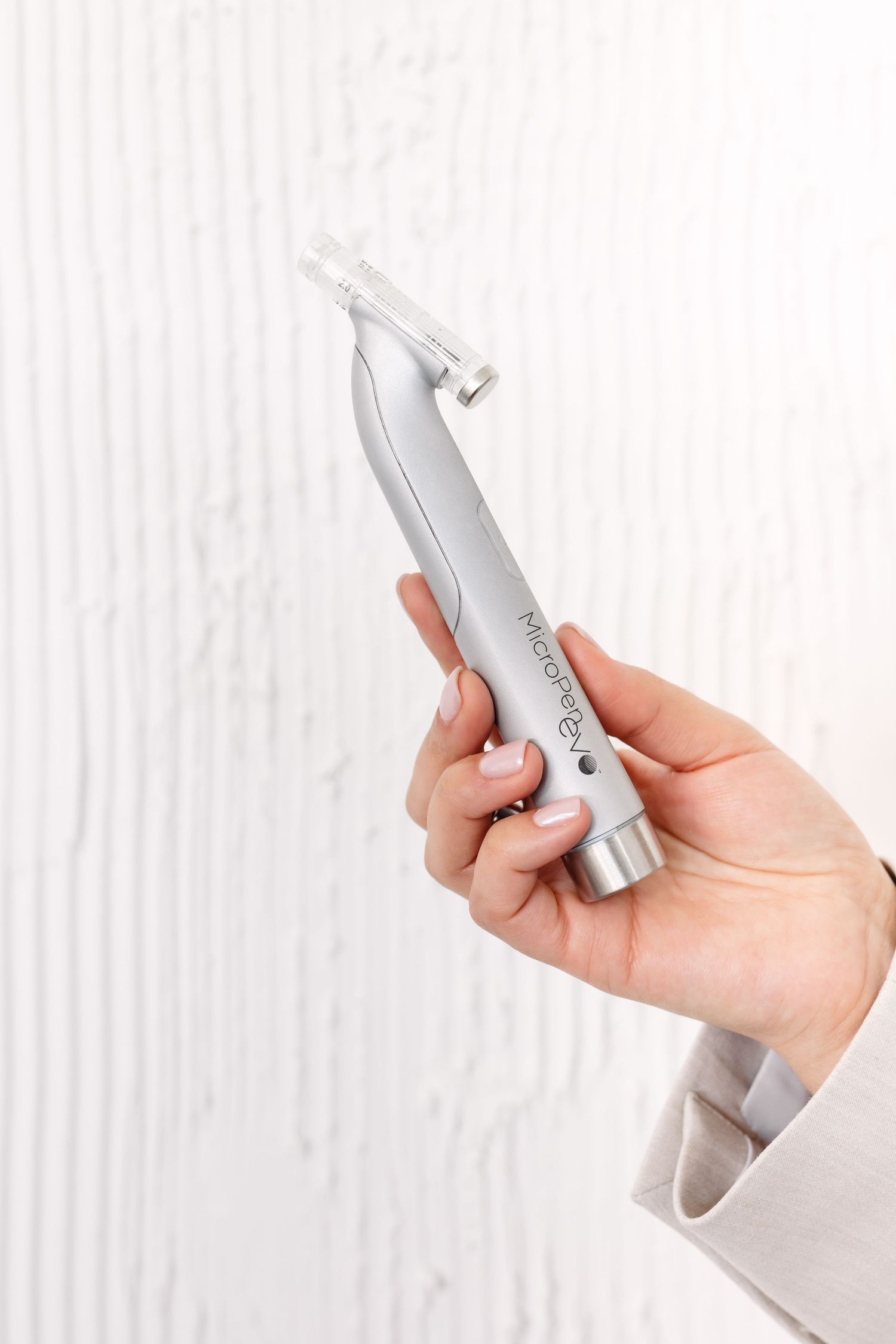 Hand holding a sleek silver dental handpiece tool against a white textured background.
