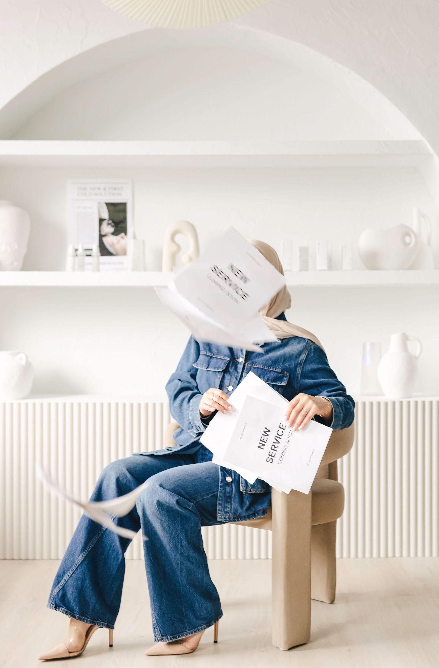 Four identical images showing jeans and a minimalist cardboard chair against a white background and wall.