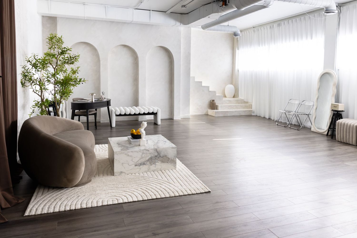 Modern minimalist living room with arched alcoves, gray sofa, marble coffee table, and dark hardwood floors in bright white space.