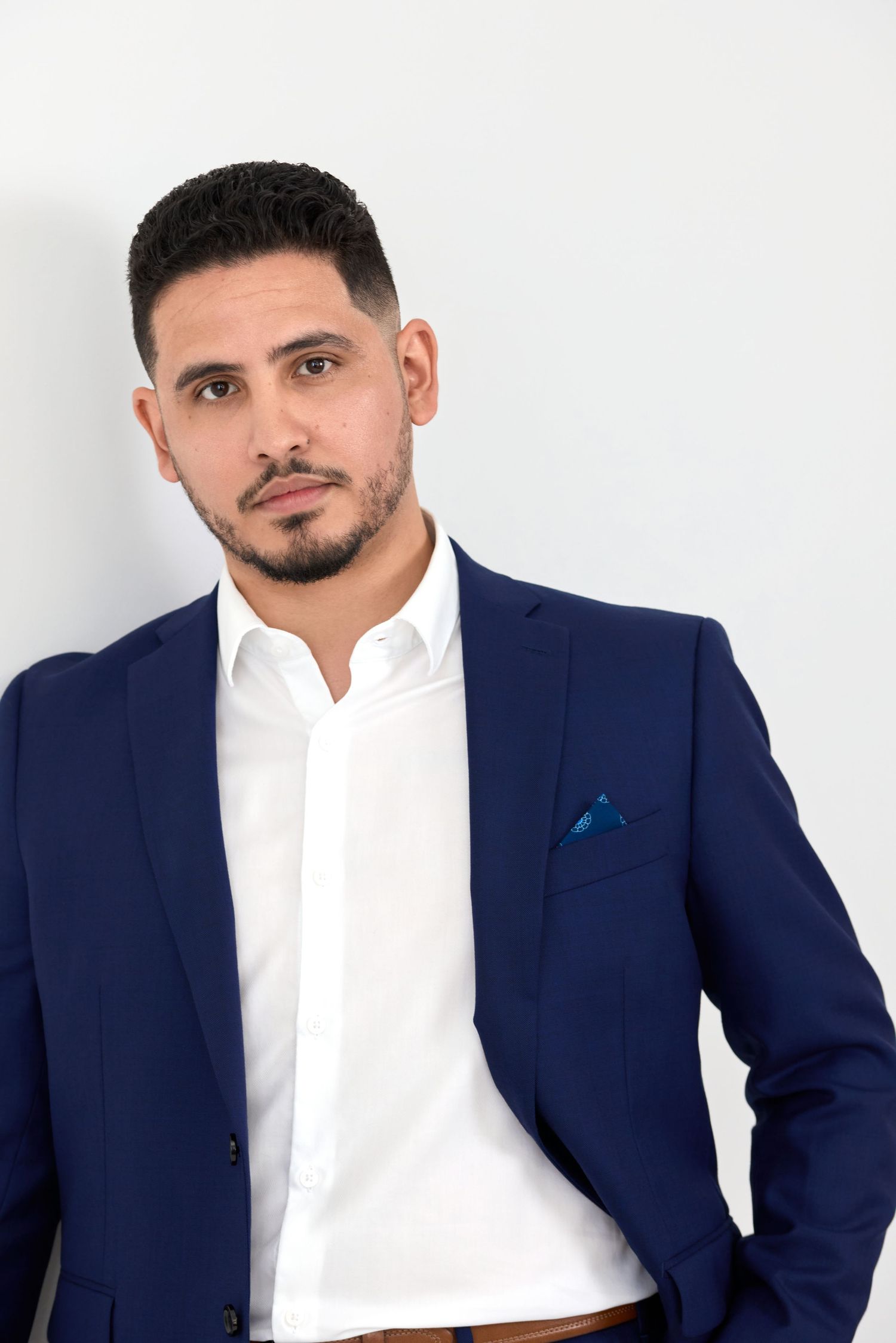 Professional studio portrait of a person in a navy blue suit and white dress shirt against a light background.
