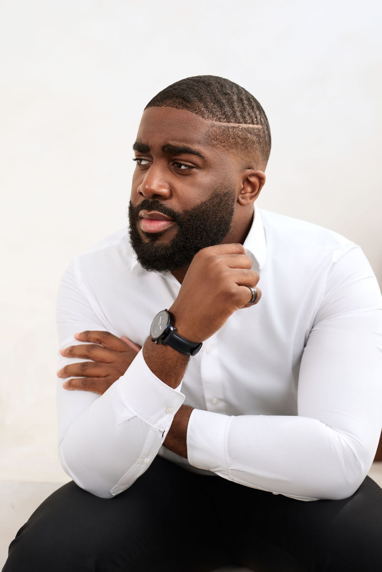 A man in a white long-sleeve shirt rests his chin on his hand while posing against a light background in three similar poses.