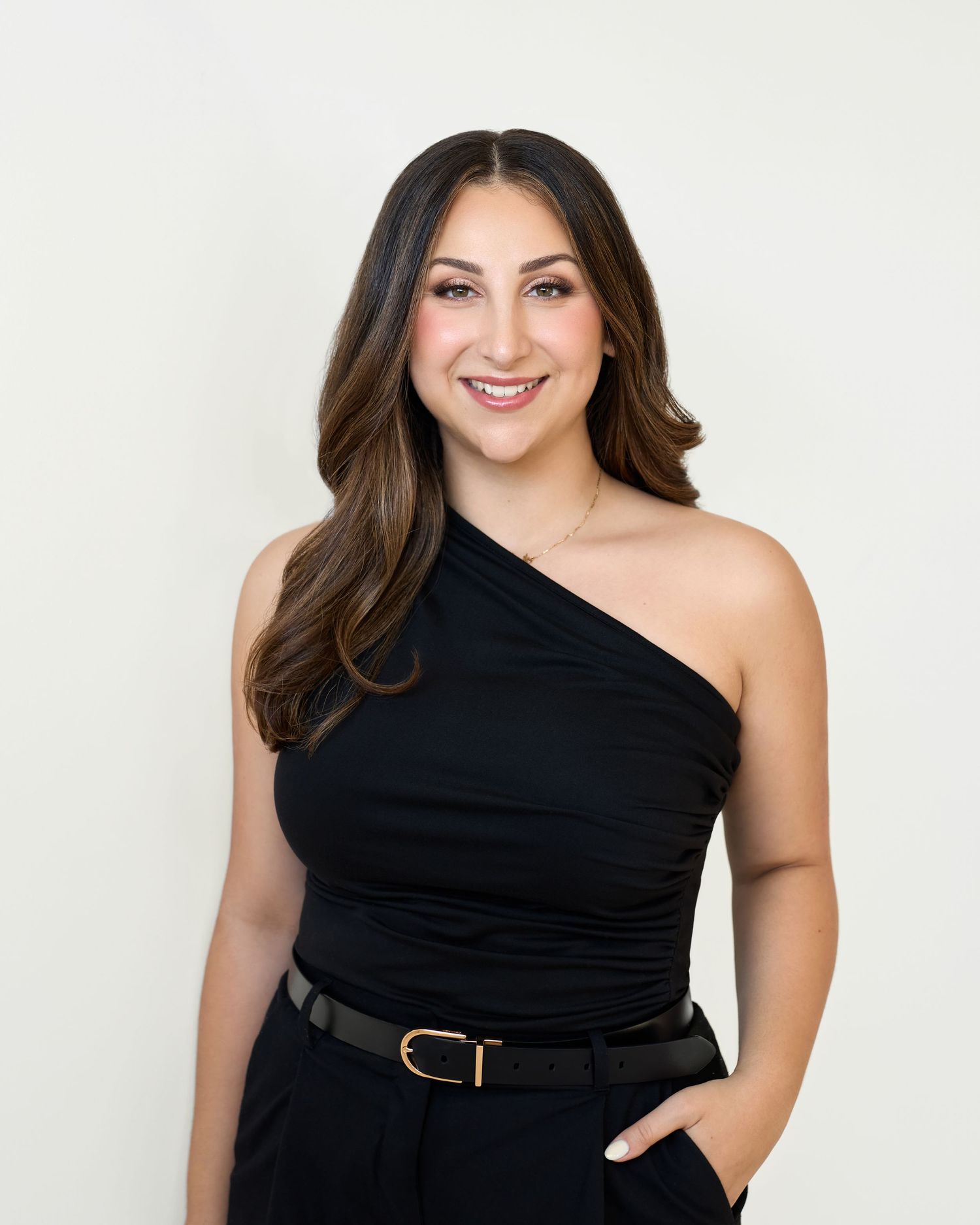 A person wearing a black one-shoulder dress poses confidently in a studio setting against a white background.