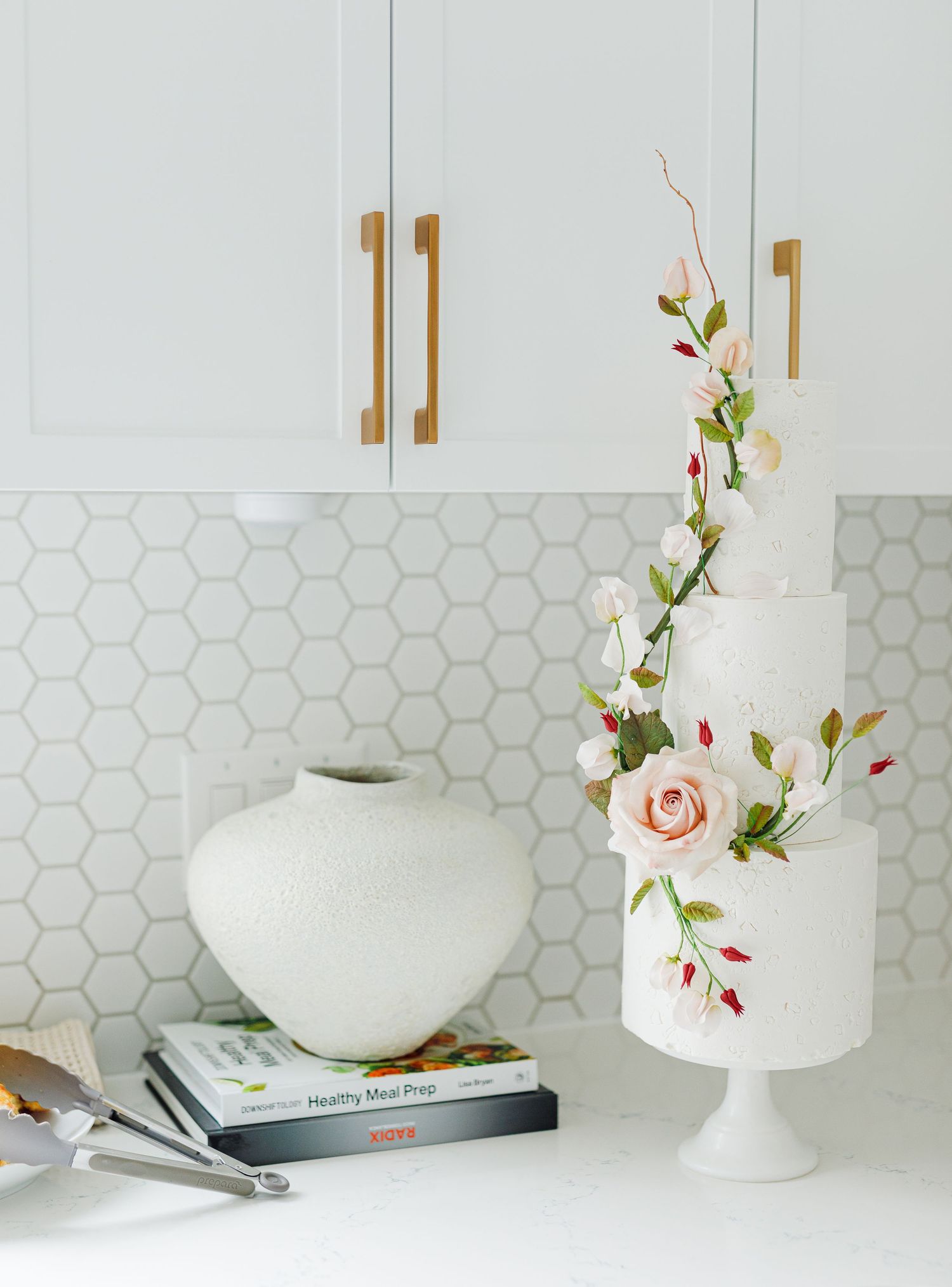 White cake stands and floral arrangements displayed on counter with hexagonal tile backsplash.