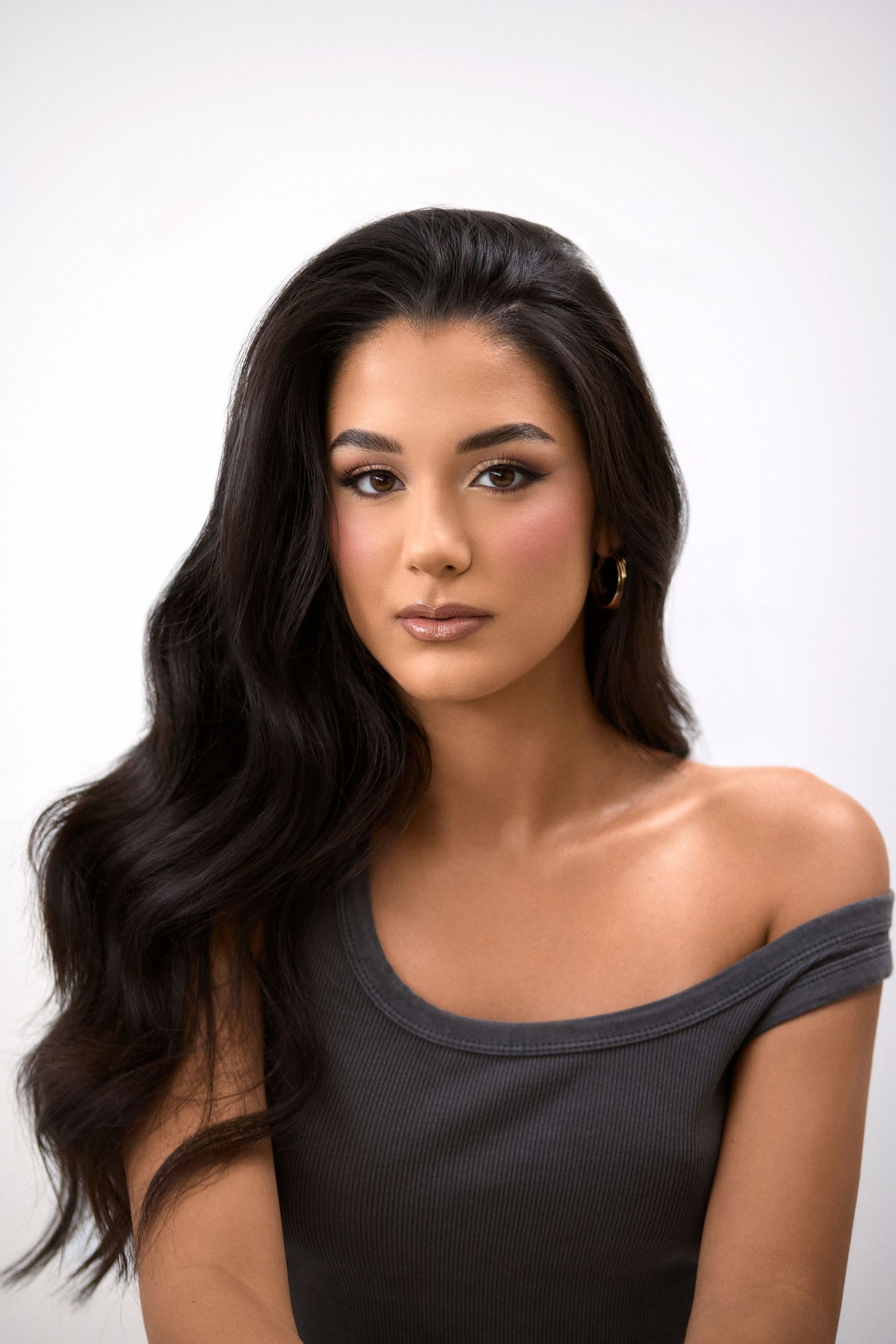 Beauty portrait featuring wavy dark hair and off-shoulder top against white background.